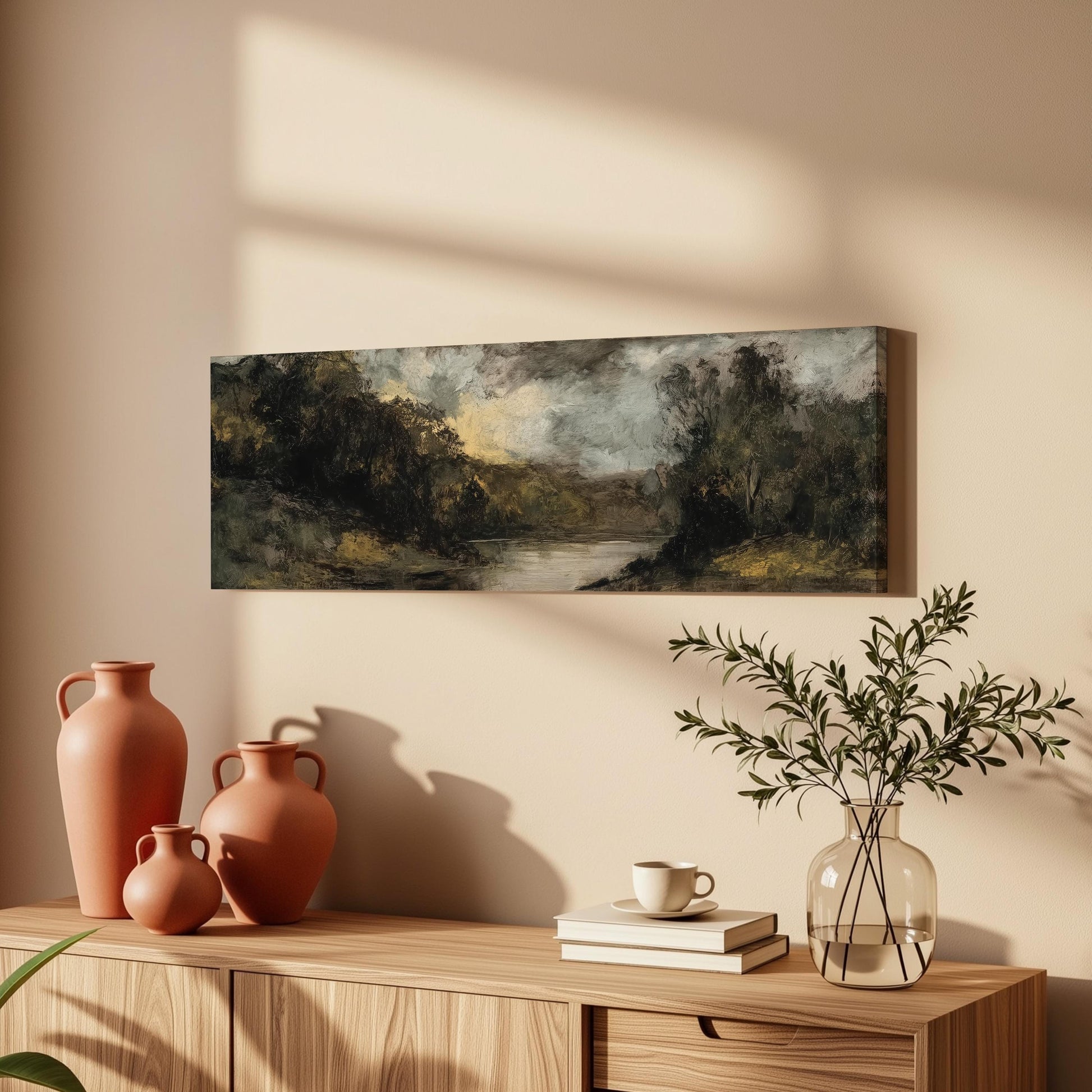 a wooden cabinet with a painting of a landscape hanging on the wall above it. The cabinet also has three orange vases and a glass vase with greenery, as well as a stack of books and a coffee cup on the surface.
