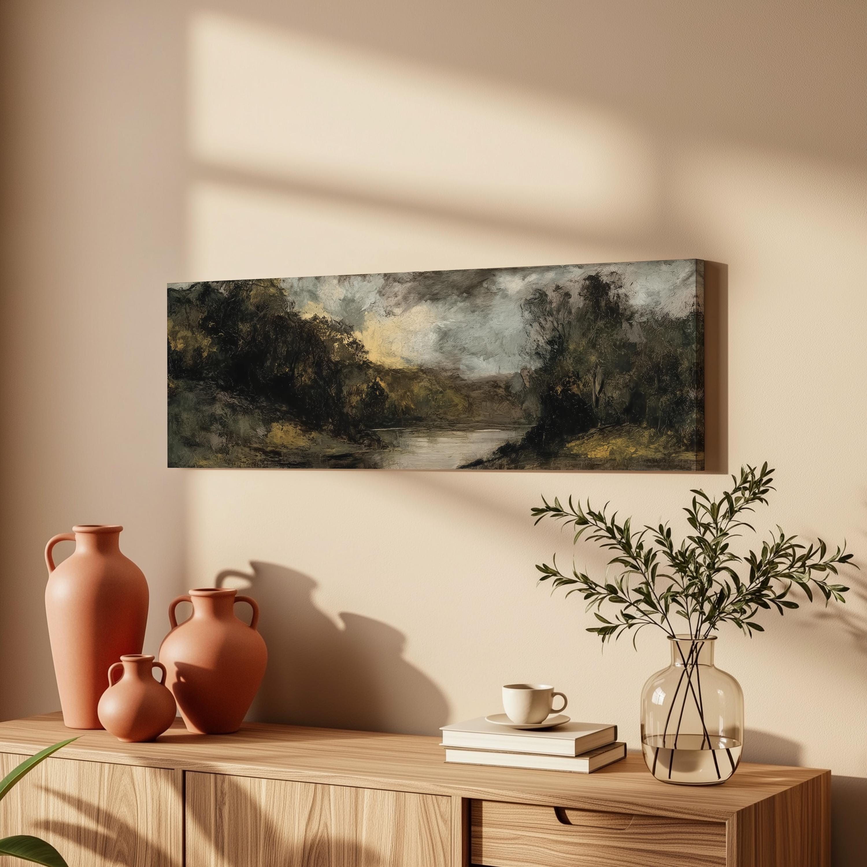 a wooden cabinet with a painting of a landscape hanging on the wall above it. The cabinet also has three orange vases and a glass vase with greenery, as well as a stack of books and a coffee cup on the surface.