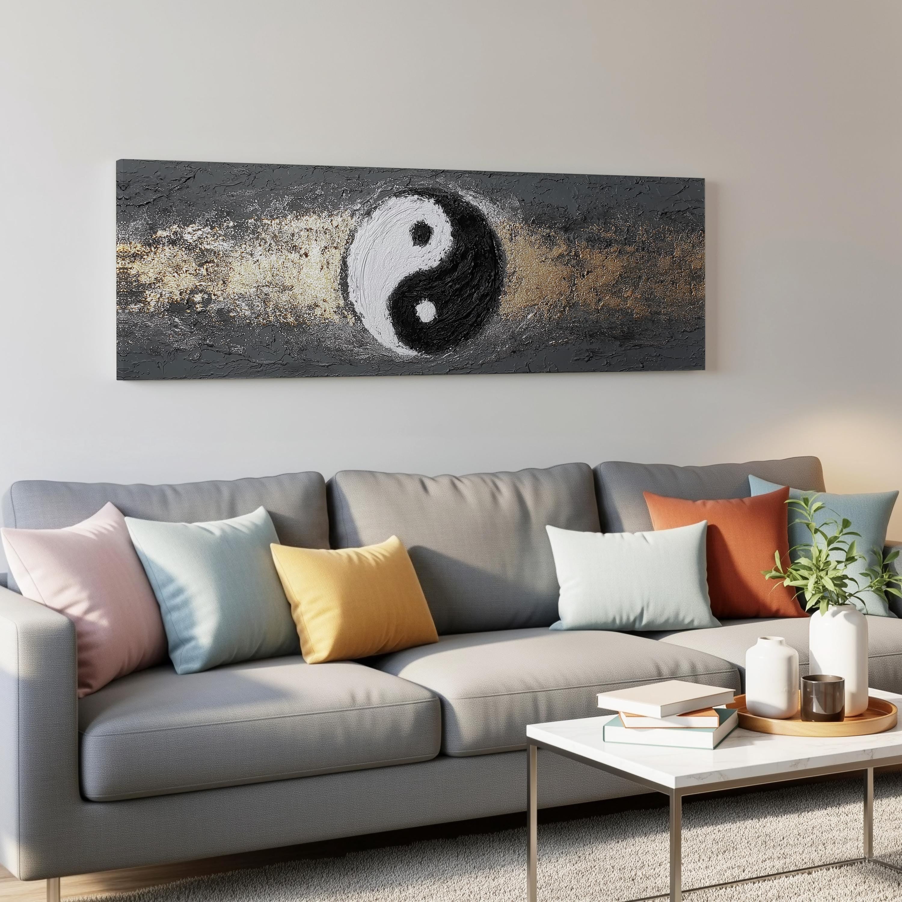 a modern living room with a gray sofa adorned with colorful throw pillows. Above the sofa, there is a large painting or artwork depicting a yin and yang symbol, which adds a unique and artistic touch to the room. The room also includes a coffee table with books and a plant, creating a cozy and inviting atmosphere.