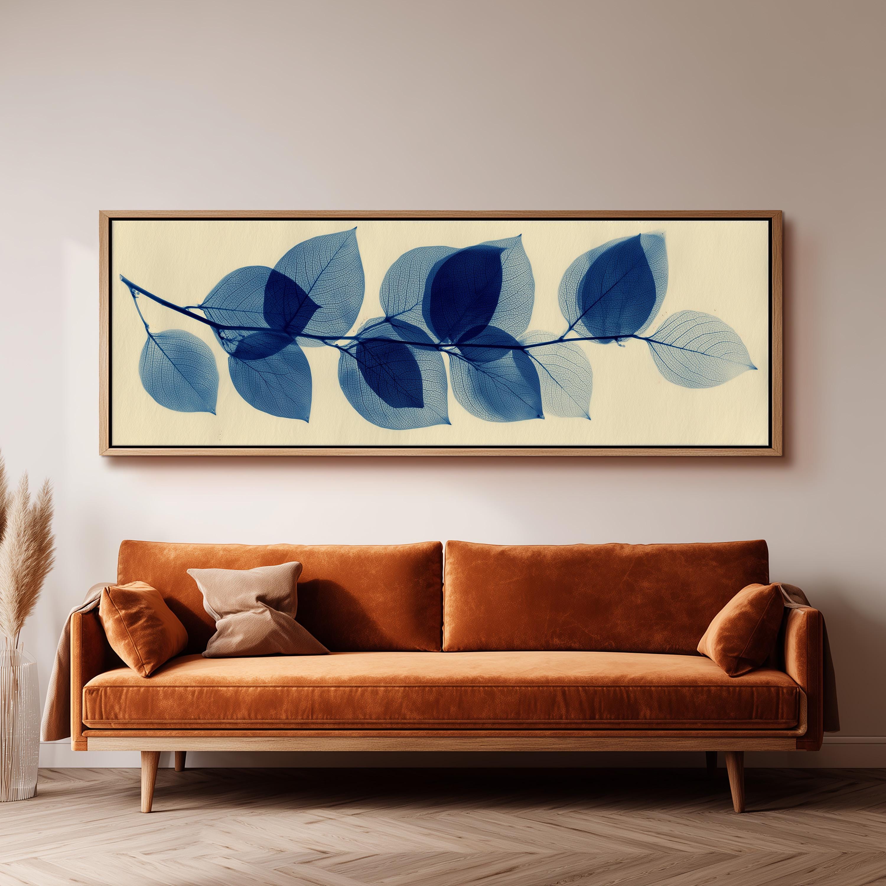 a large framed artwork of blue leaves hanging on a wall above a brown sofa in a living room setting.