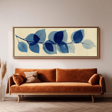 a large framed artwork of blue leaves hanging on a wall above a brown sofa in a living room setting.