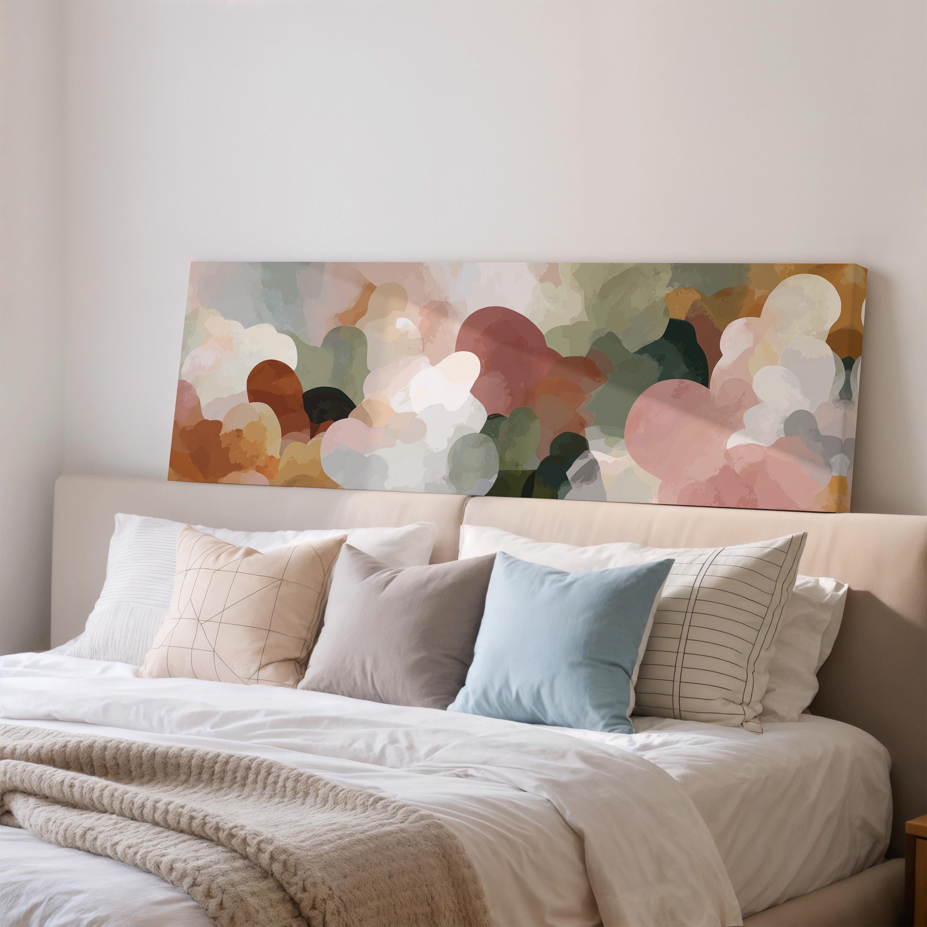 a large bed with a white comforter and various pillows, including a blue pillow and a striped pillow. Above the bed, there is a large abstract painting or artwork displayed on the wall.
