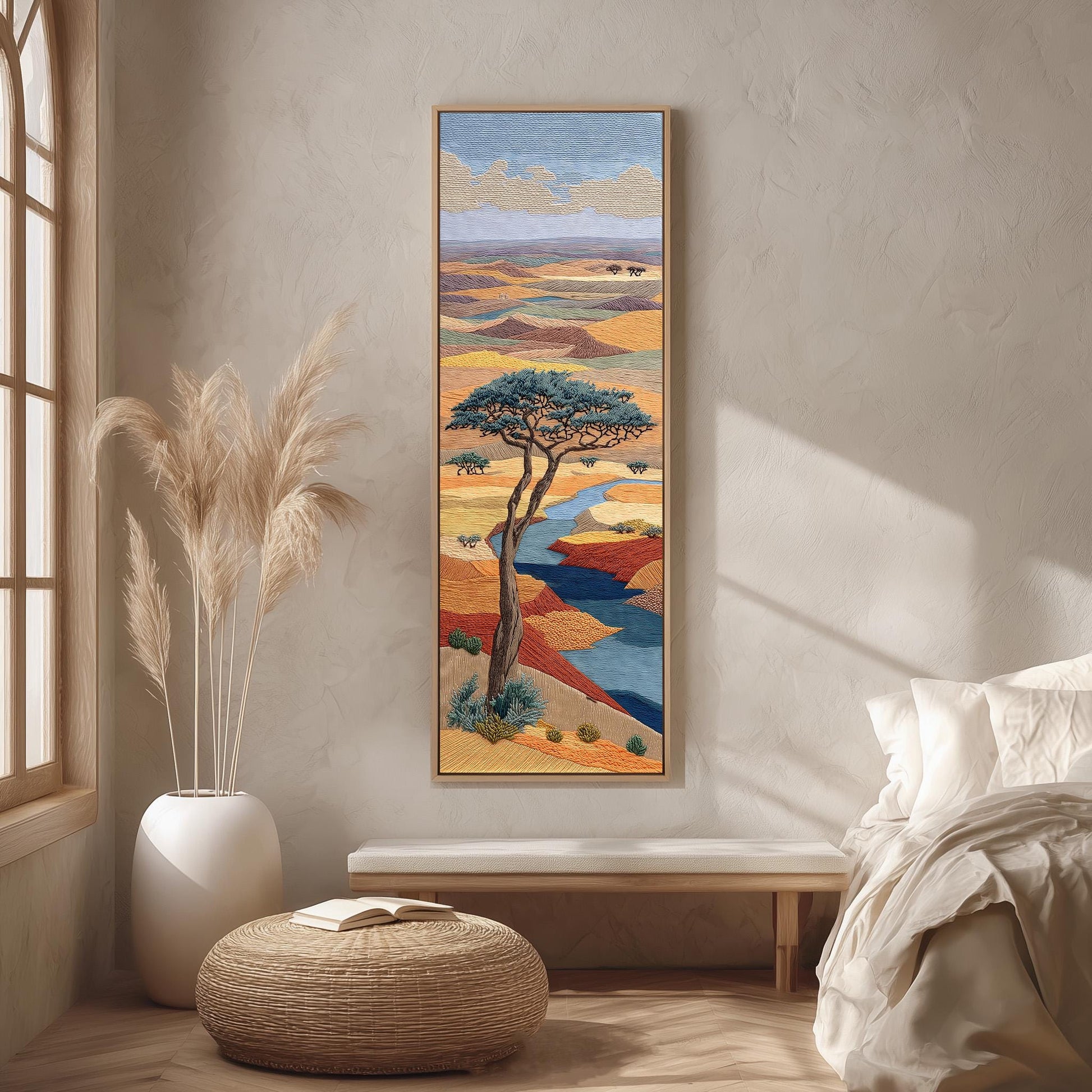 a large painting of a tree in a desert landscape hanging on a wall in a room with a bed, a window, and a woven ottoman.