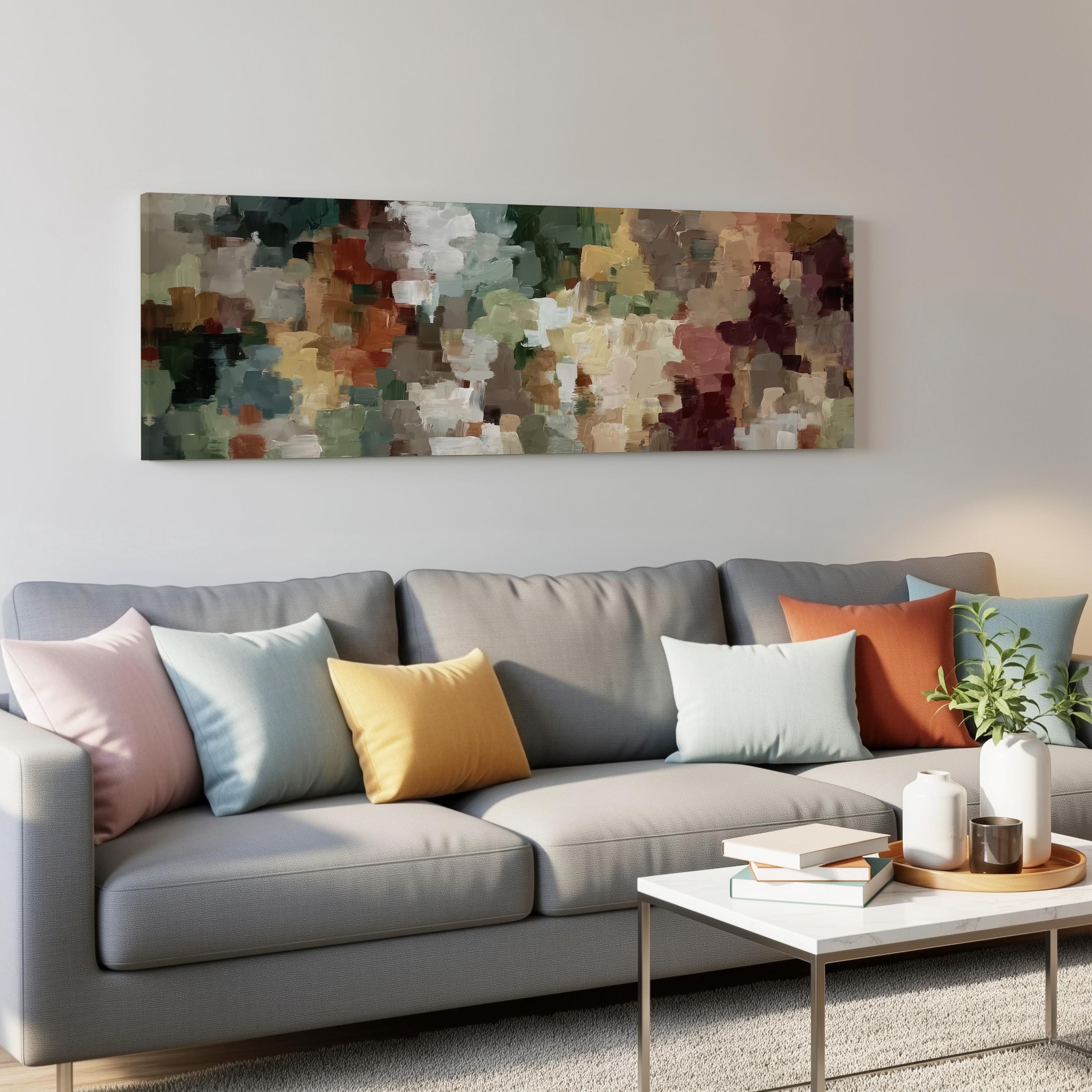 a modern living room with a gray sofa adorned with colorful throw pillows. Above the sofa, there is a large abstract painting hanging on the wall. In front of the sofa, there is a white coffee table with a stack of books and a small plant.