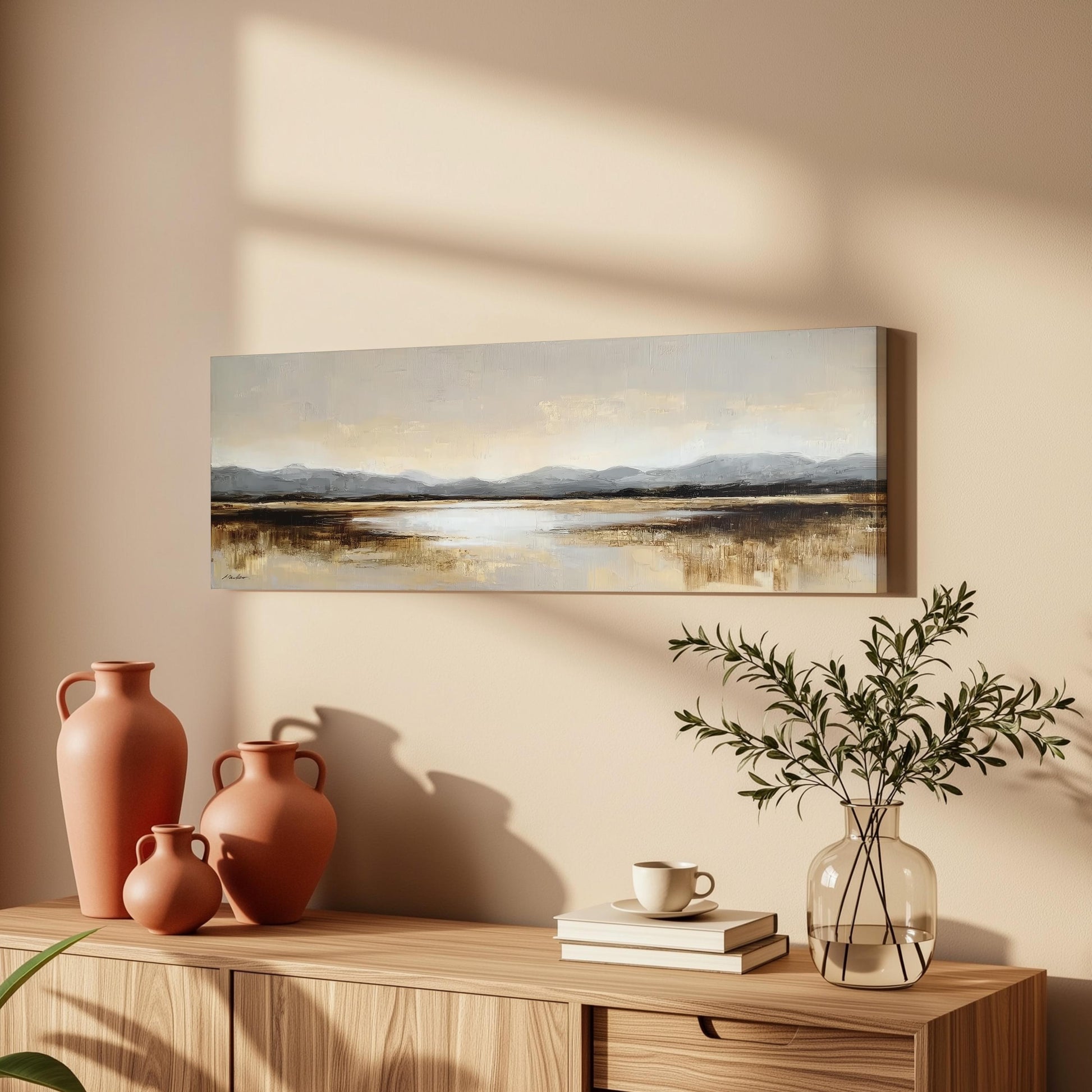 a wooden cabinet with a painting of a landscape hanging on the wall above it. The cabinet also has three orange vases and a glass vase with greenery, as well as a stack of books and a coffee cup on the surface.