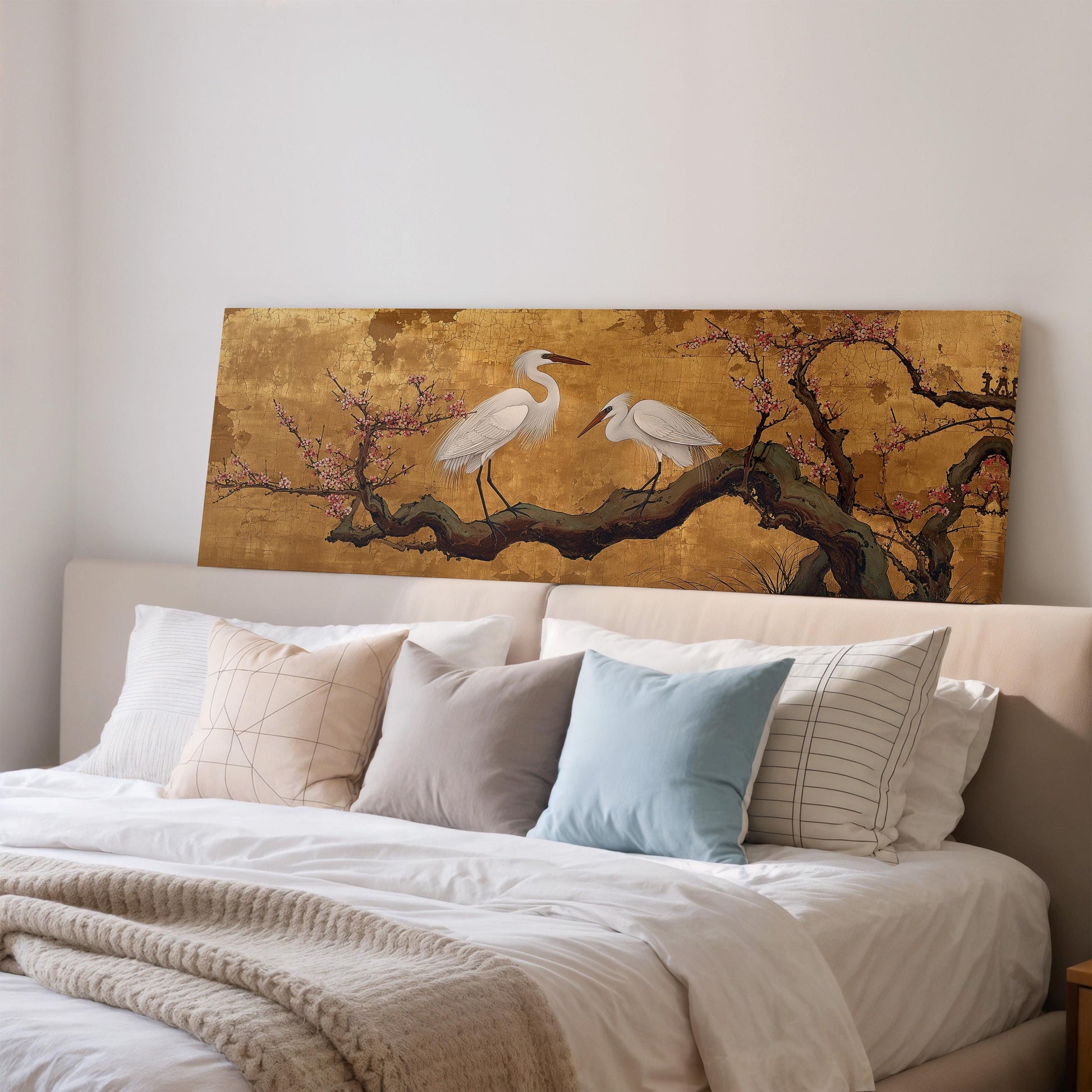 a large painting of two white birds perched on a branch, which is displayed on a wall above a bed with white pillows and a gray blanket.