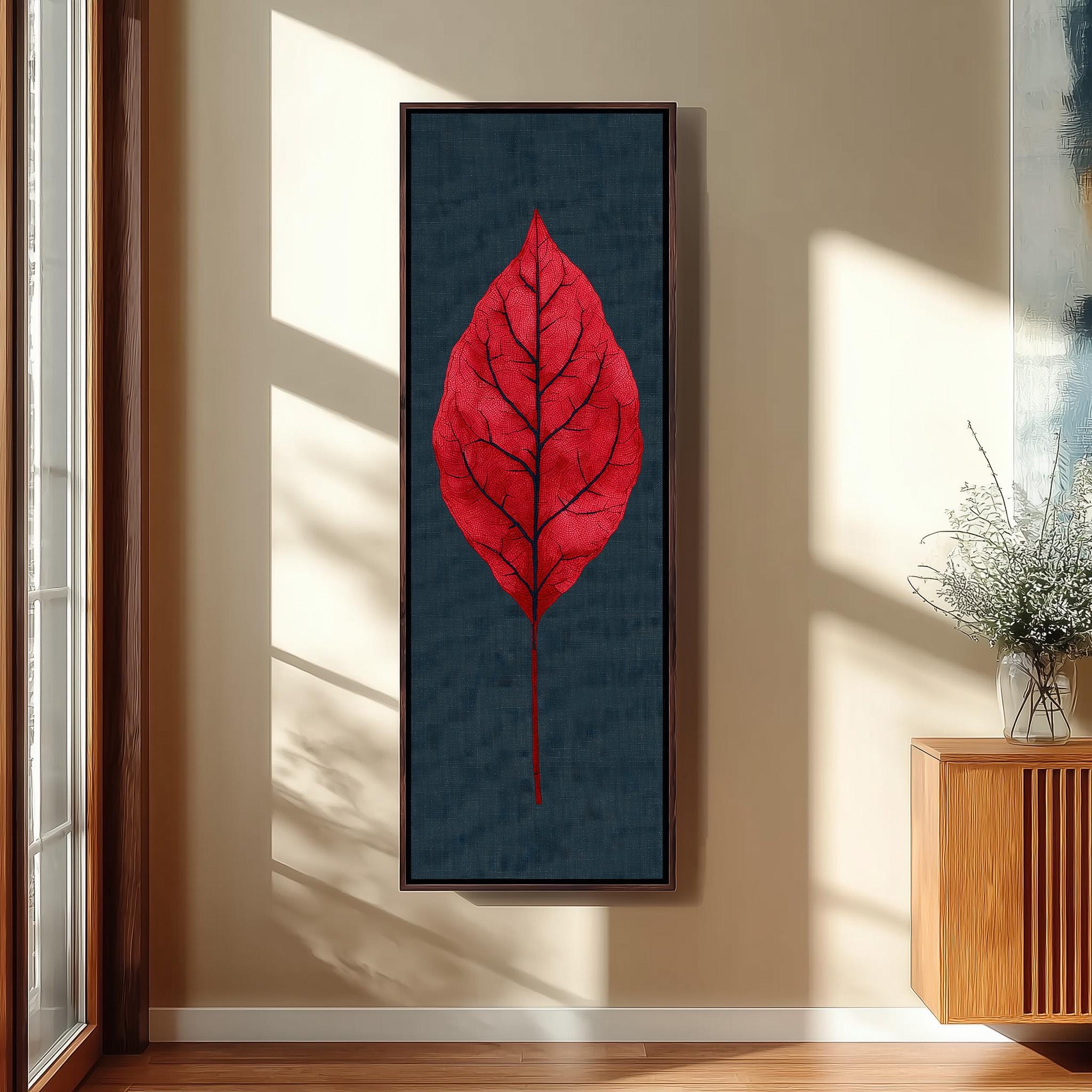 a large framed artwork of a red leaf on a wall, with a wooden cabinet and a vase of greenery to the right.