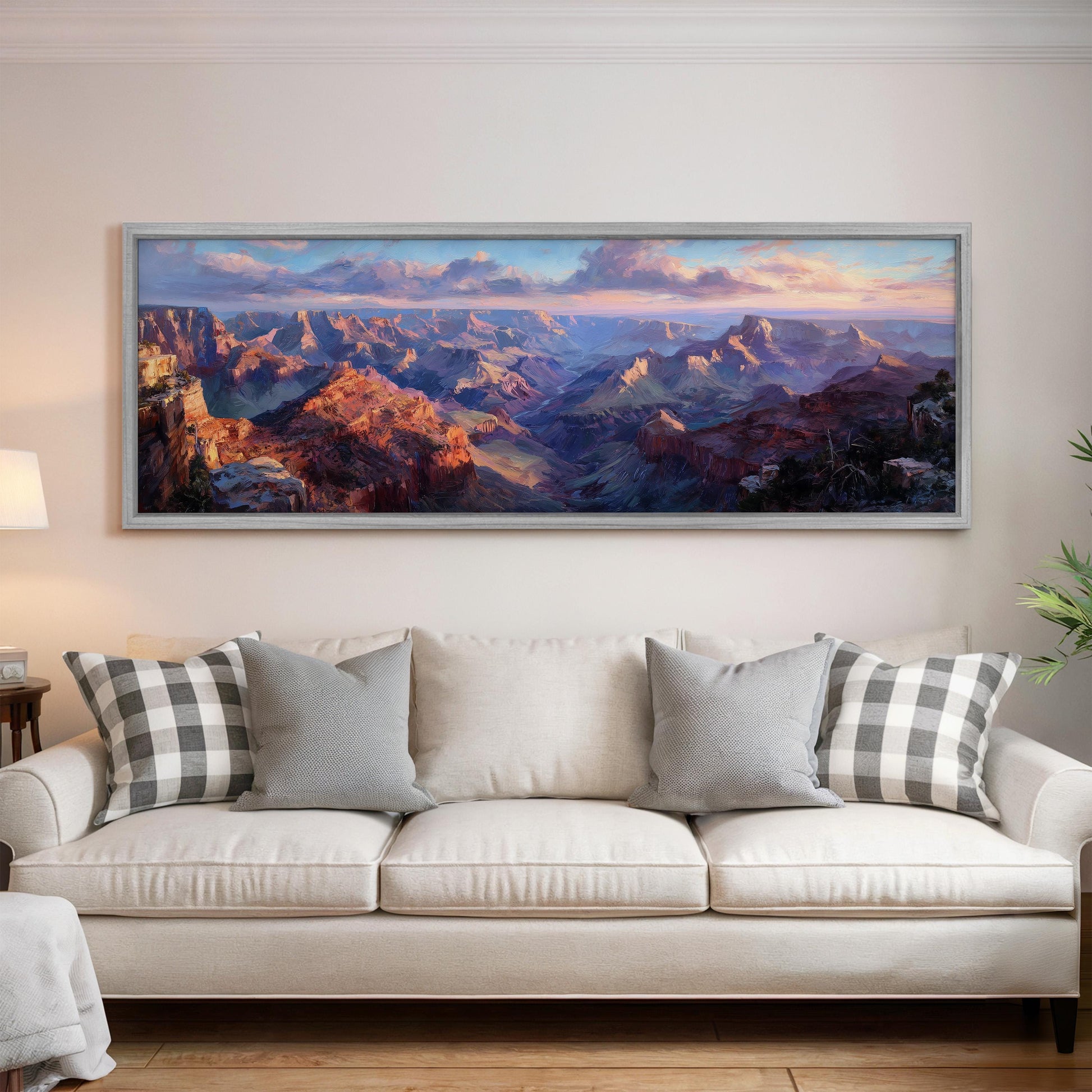a large, framed painting of a mountainous landscape hanging on a wall above a white couch with patterned throw pillows.