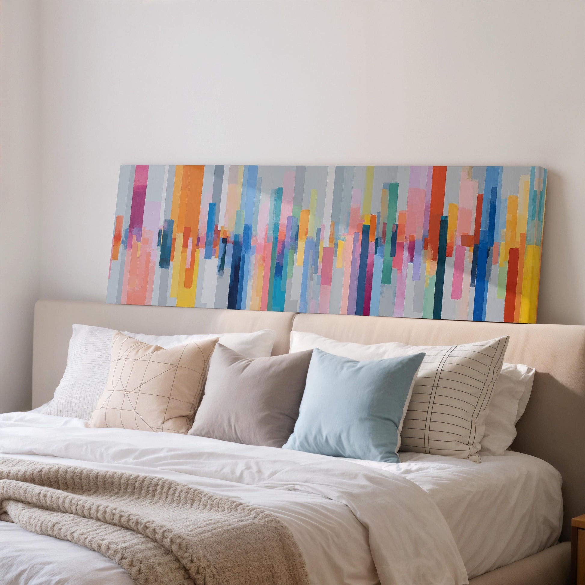 a large bed with a white comforter and a variety of colorful pillows. The bed is set against a wall with a large abstract painting hanging above it.