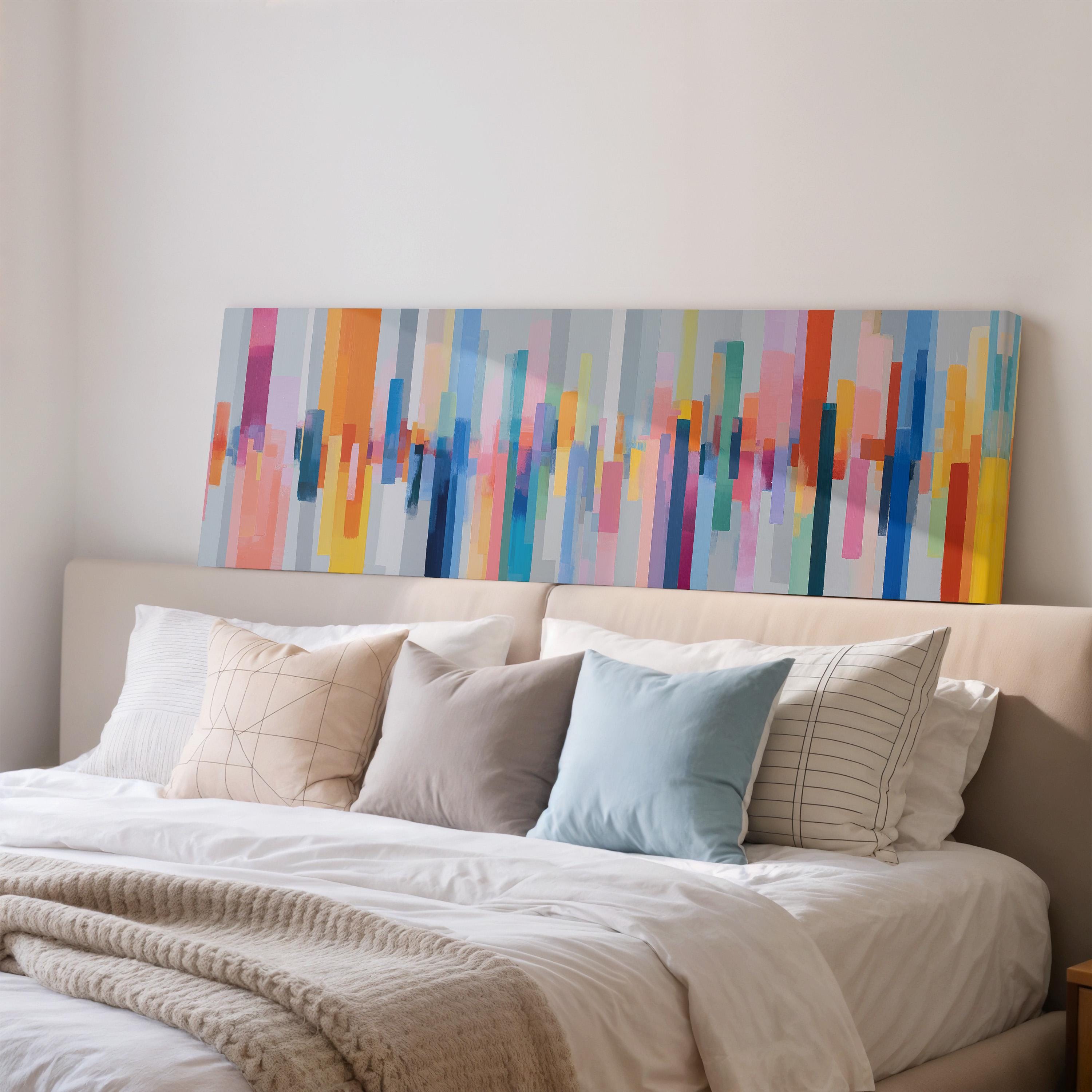 a large bed with a white comforter and a variety of colorful pillows. The bed is set against a wall with a large abstract painting hanging above it.