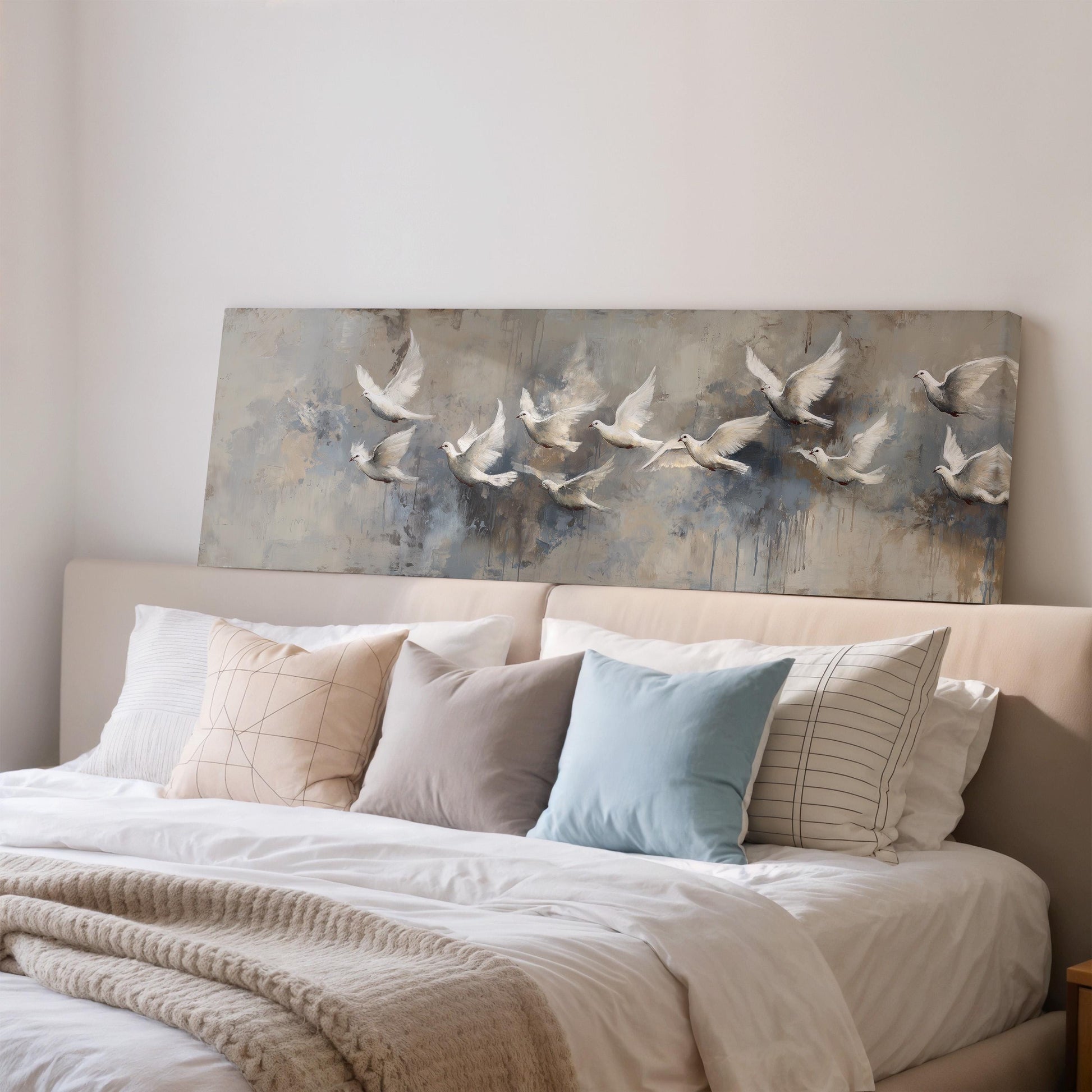 a cozy bedroom scene with a large bed adorned with white linens and a variety of colorful pillows. Above the bed, there is a painting of a flock of white birds in flight, adding a touch of nature and serenity to the room.