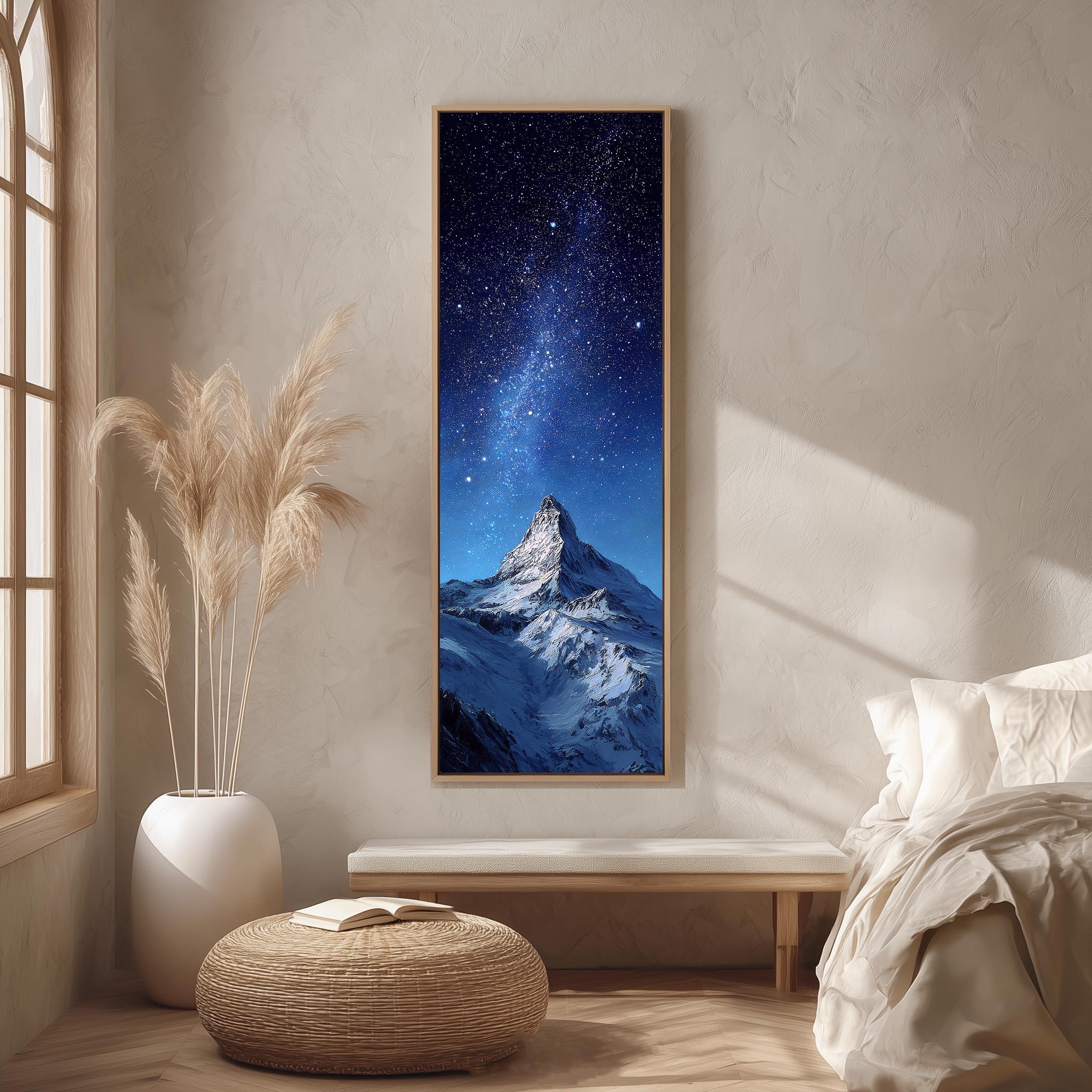 a serene bedroom setting with a large framed picture of a snowy mountain peak under a starry night sky hanging on the wall. The room has a white bed, a wicker ottoman, and a potted plant, creating a cozy and inviting atmosphere.