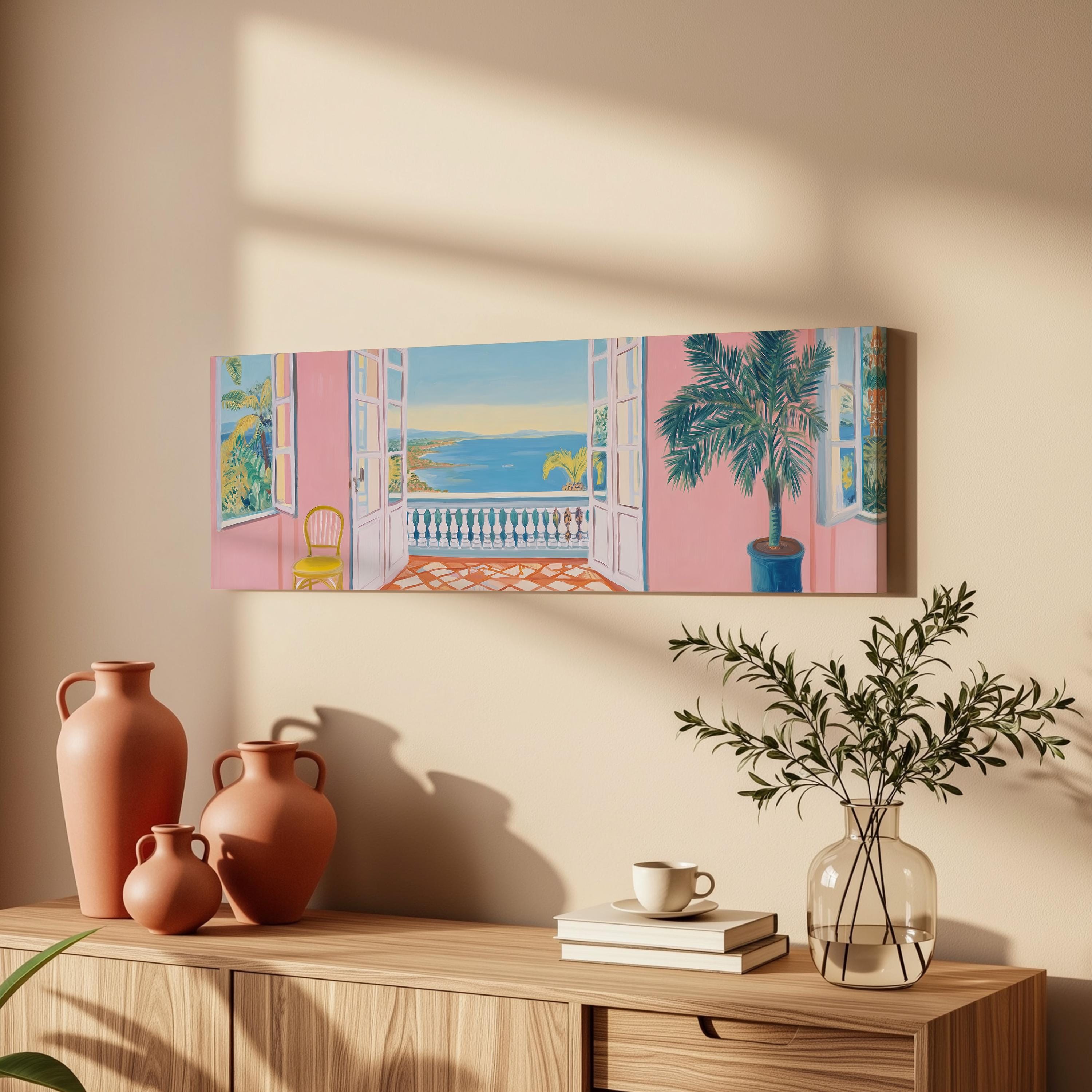 a painting of a balcony with a palm tree, a pink wall, and a blue sky with a yellow sun. The painting is hung on a wall above a wooden dresser with a vase, a plant, and a stack of books.
