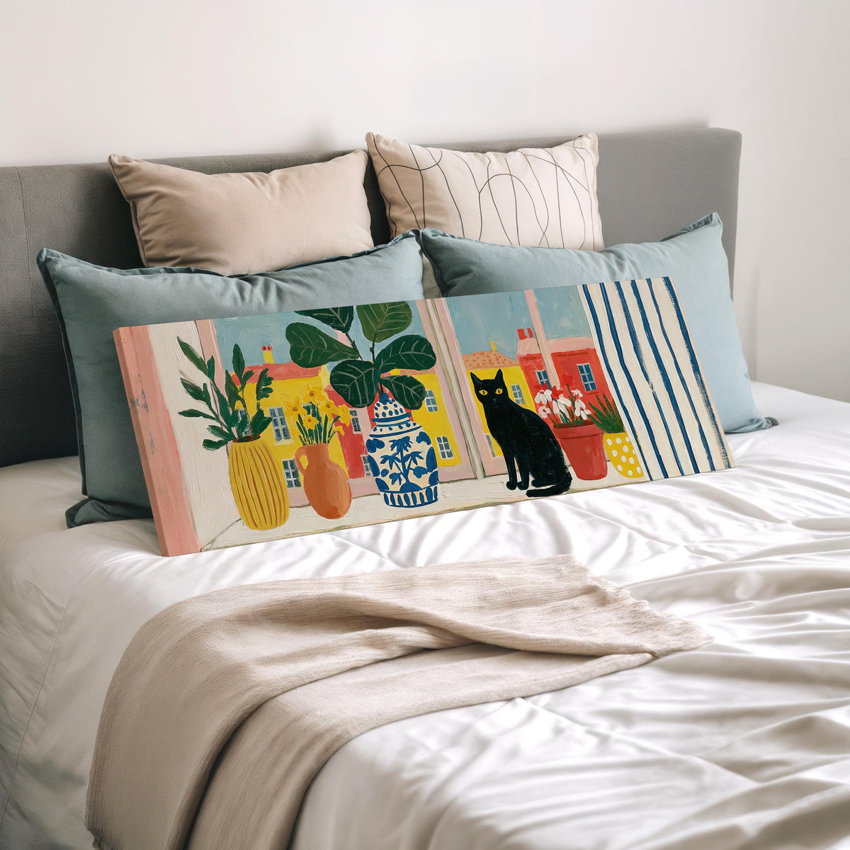 Black cat on a windowsill overlooking a colorful village wide panoramic canvas print laid on a bed to show its size