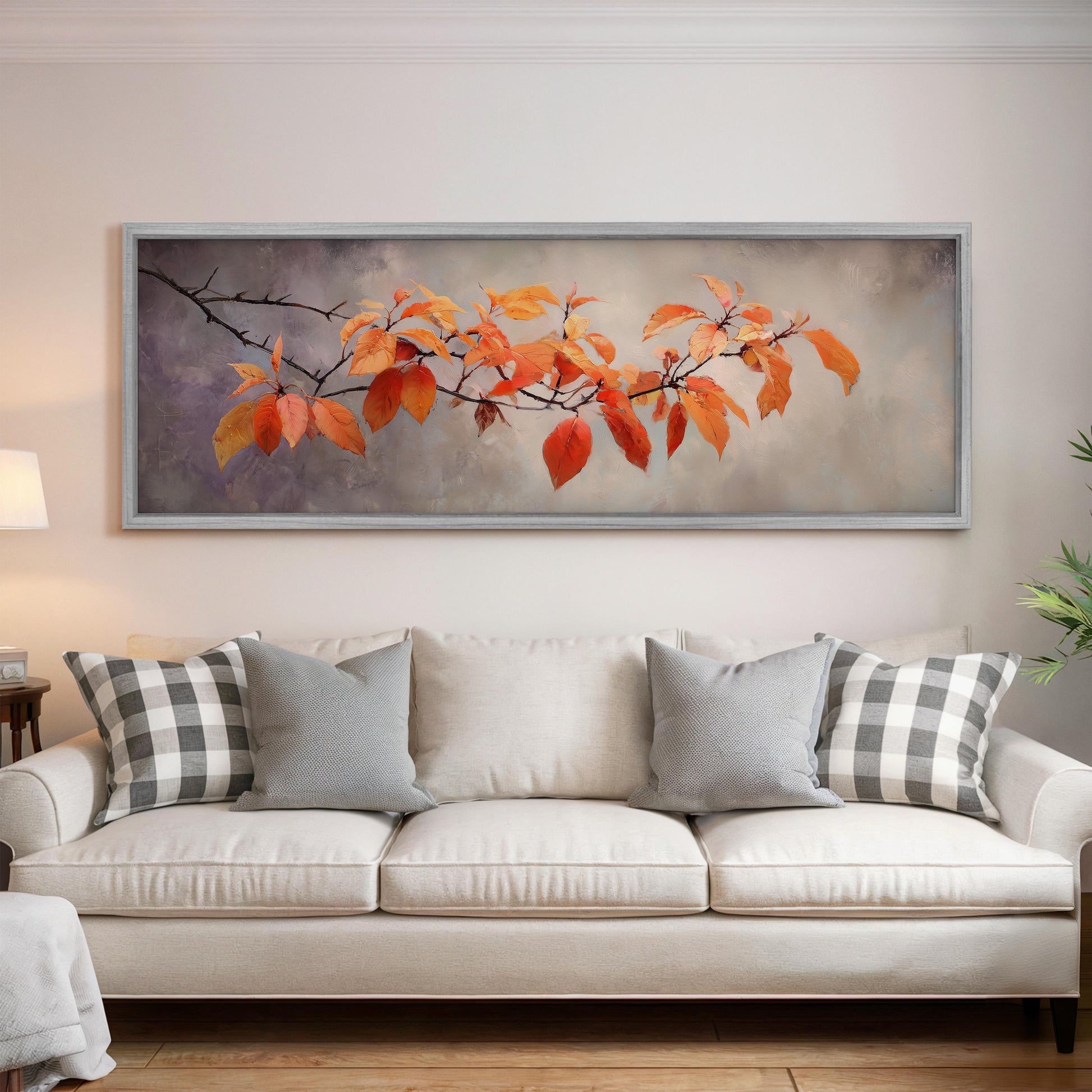 a large painting of orange leaves hanging on a wall above a white couch with gray and white pillows.