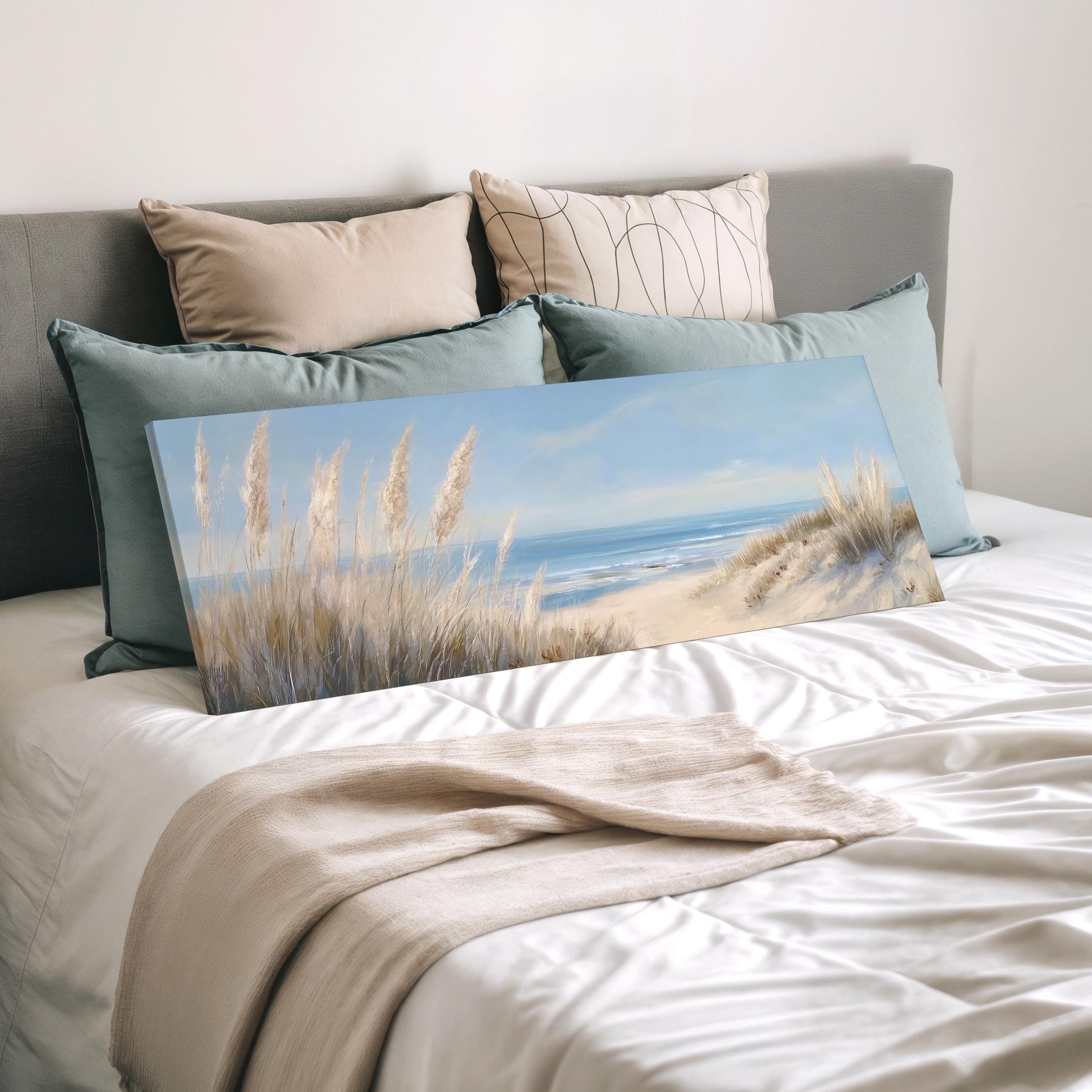 a bedroom with a bed and a painting of a beach scene on it. The bed has a white comforter and is decorated with several pillows. The painting depicts a serene beach landscape with tall grasses and a calm ocean in the background.