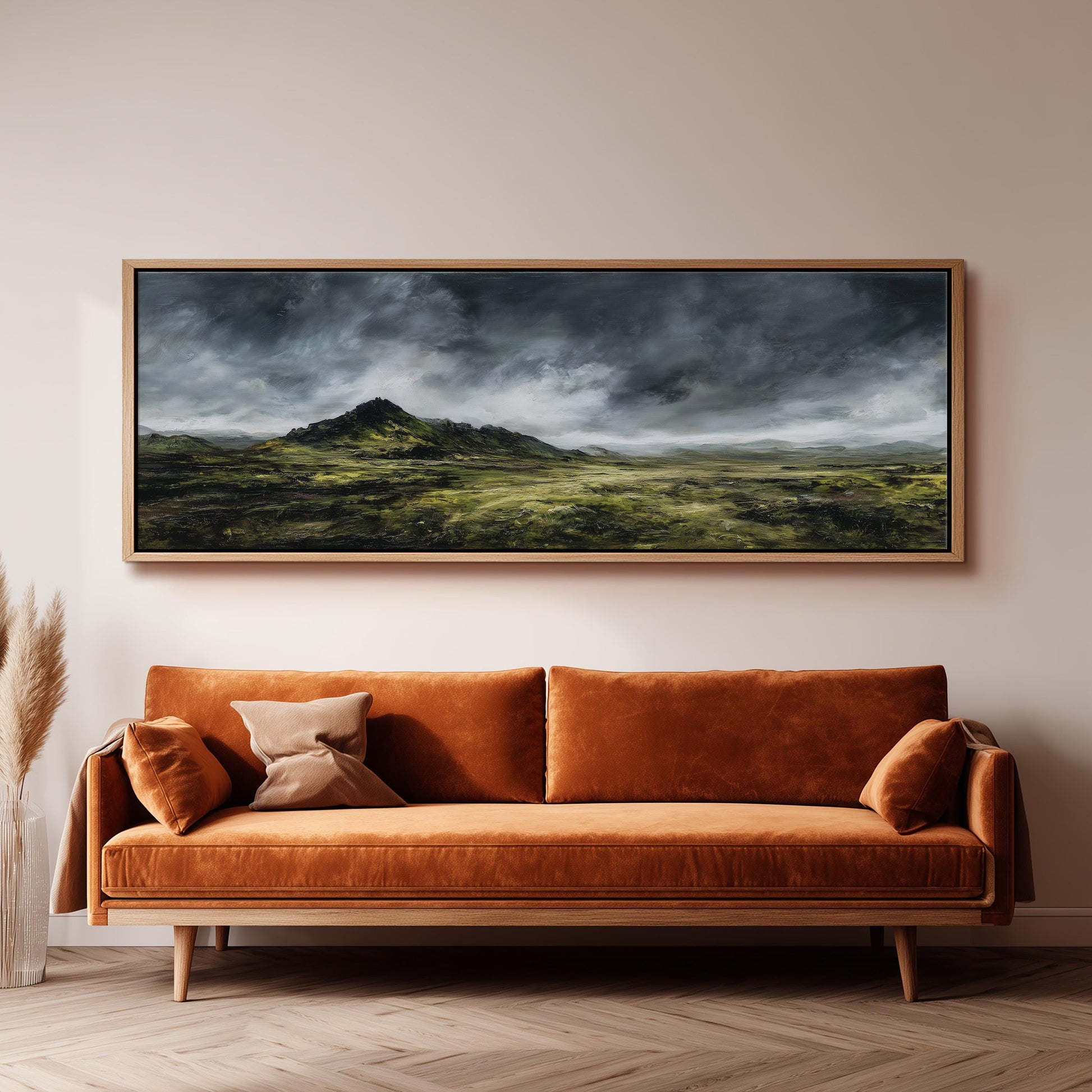 a large landscape painting hanging on a wall above a brown sofa with orange cushions.