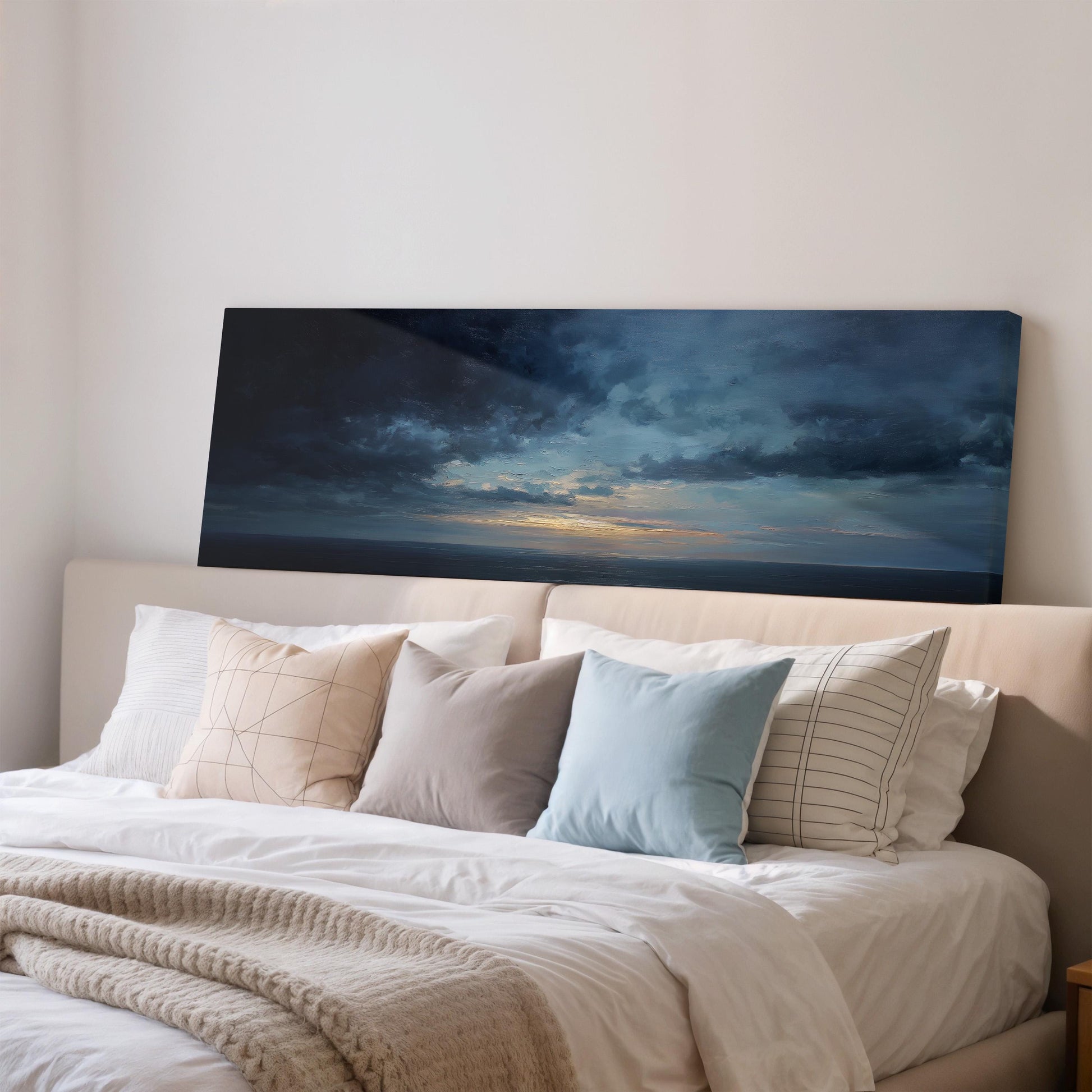 a bedroom with a large bed covered in white sheets and pillows. Above the bed, there is a large canvas print depicting a dramatic sky with clouds and a sunset.