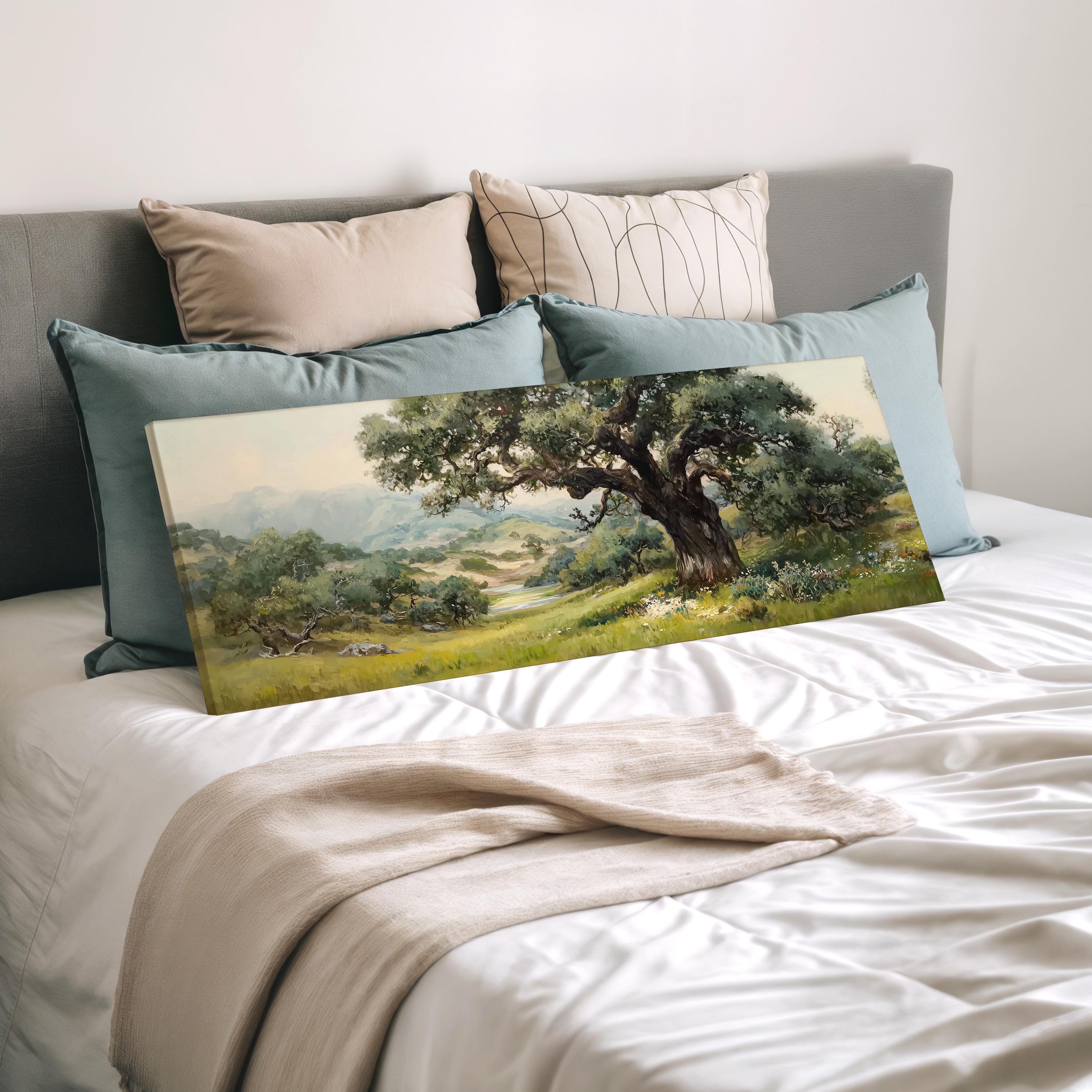 a large landscape painting displayed on a bed, with a beige blanket and pillows surrounding it.