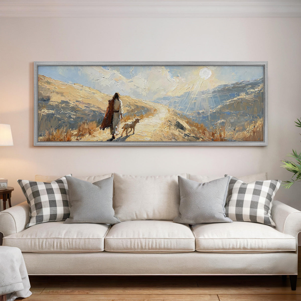 Jesus walking a sunlit hillside path with a sheep panoramic canvas print above a white sofa in a bright living room