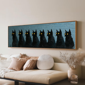 Row of black cats with glowing eyes long horizontal canvas print above a sofa in a living room