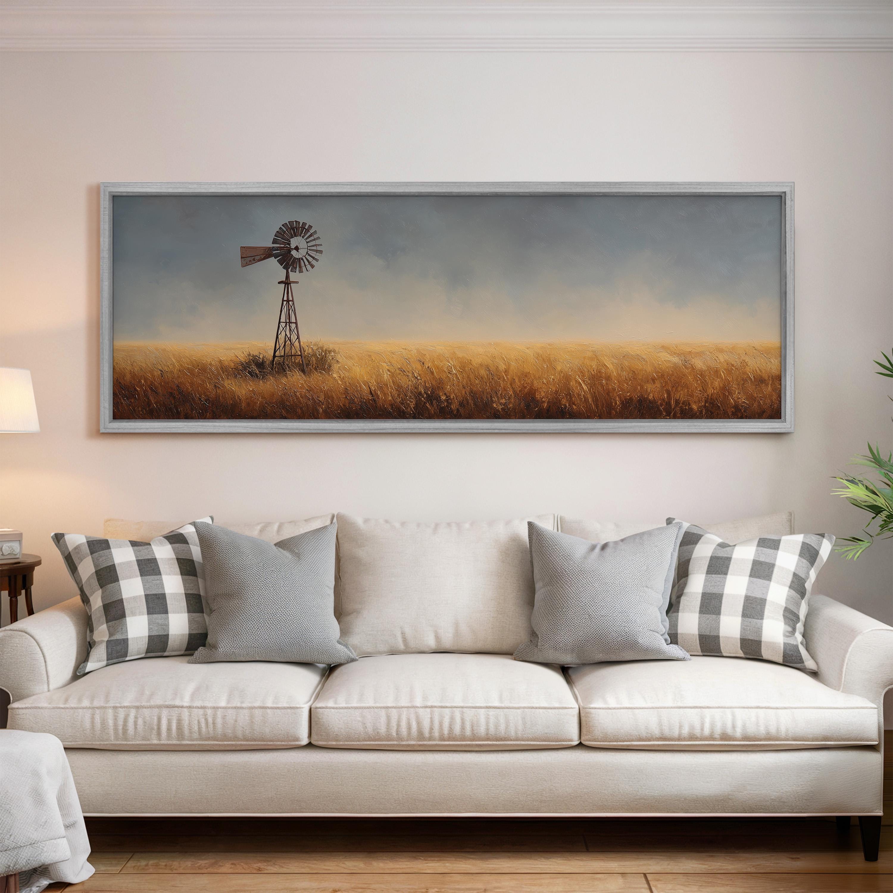 a large painting of a windmill in a field, hanging on a wall above a white couch with gray and white plaid throw pillows.