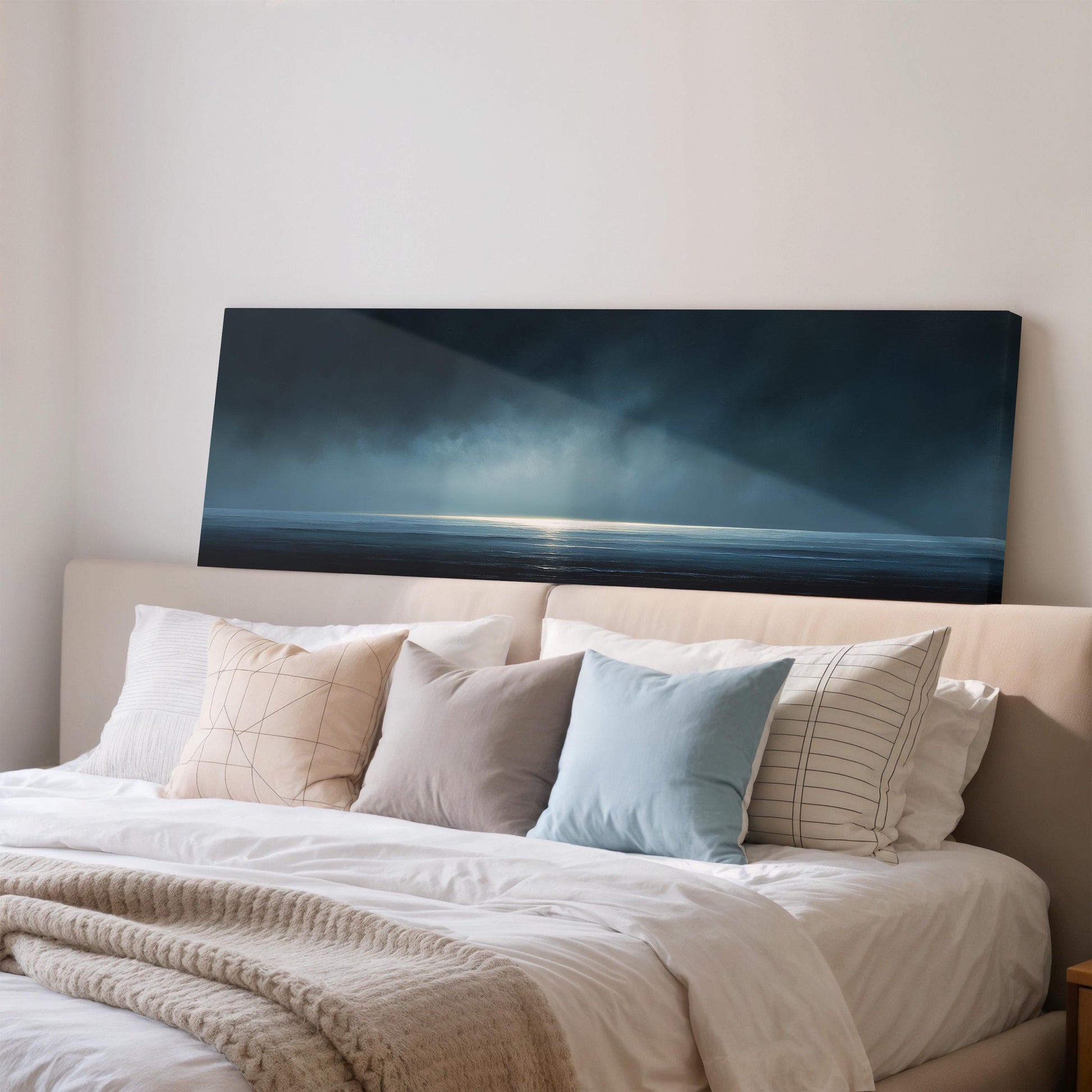 a bedroom with a large bed covered in white sheets and pillows. Above the bed, there is a large canvas print depicting a serene landscape with a body of water and a sky filled with clouds.