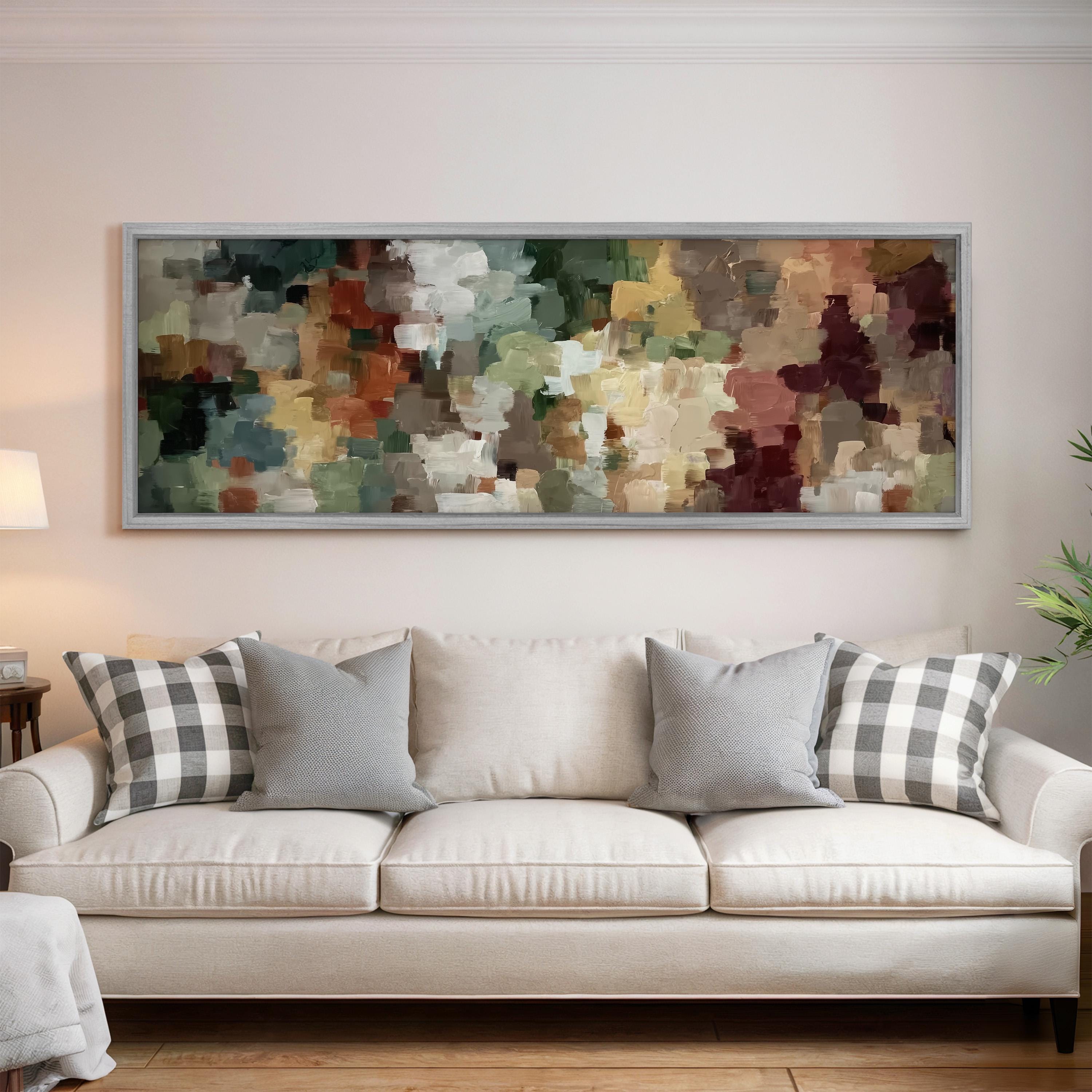 a large abstract painting hanging on a wall above a white sofa with gray and white plaid throw pillows.