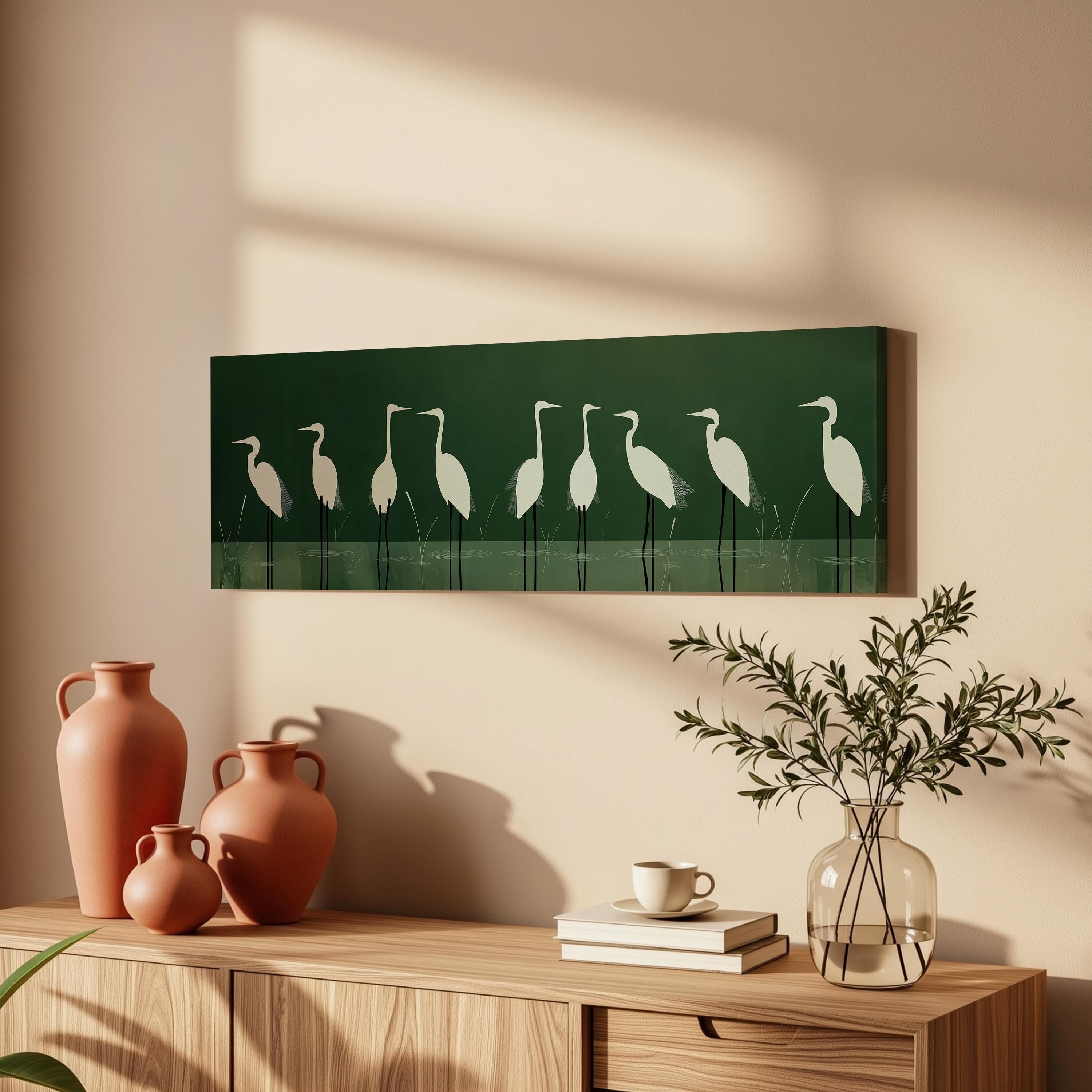 a wooden cabinet with a vase, a coffee cup, and a stack of books on top. Above the cabinet, there is a framed artwork of white birds on a green background.