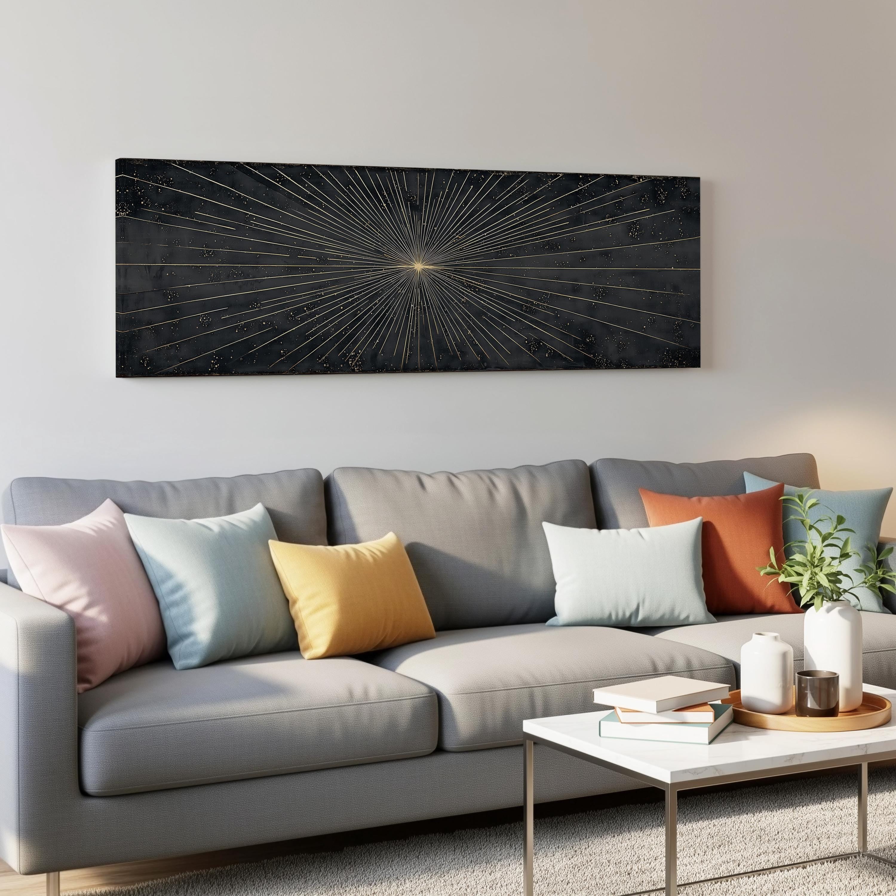 a modern living room with a gray sofa adorned with colorful throw pillows. Above the sofa, a large black and gold abstract painting hangs on the wall, adding a striking visual element to the space. In front of the sofa, there is a white coffee table with a stack of books and a small plant, creating a cozy and inviting atmosphere.