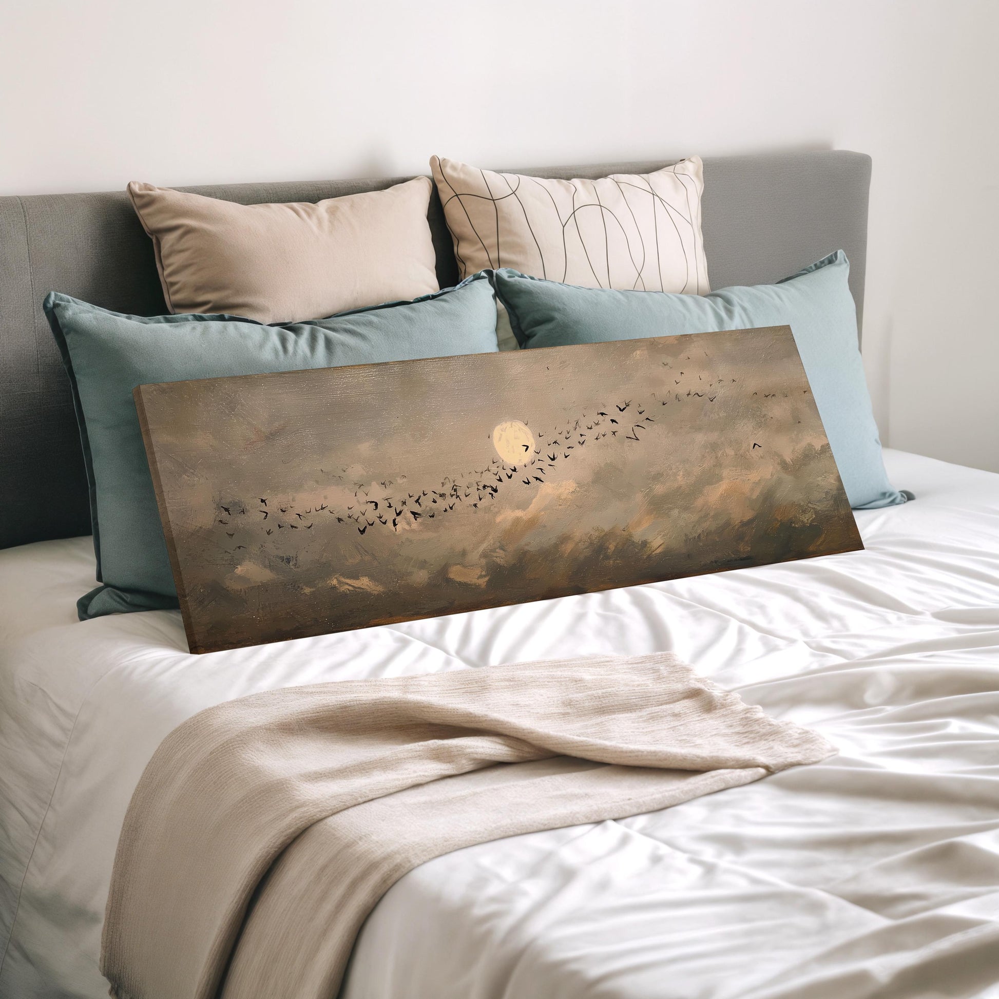 a bedroom with a bed and a painting of a flock of birds on the bed. The bed is covered with white sheets and has several pillows on it. The painting is placed on the bed, and the bed appears to be made up neatly.