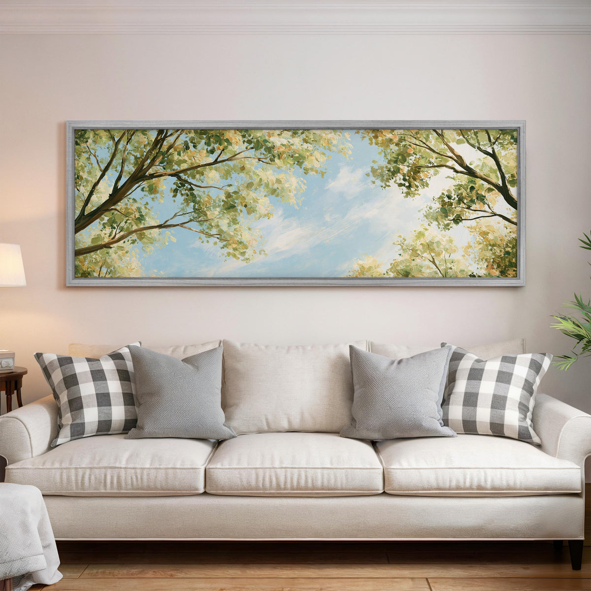 Sunlit leafy branches framing soft clouds panoramic canvas print above a white sofa in a bright living room