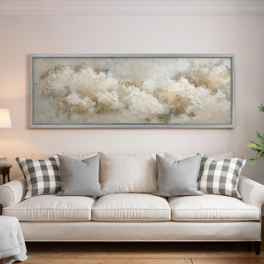 a living room with a large, framed painting of clouds hanging above a white sofa with gray and white plaid throw pillows.