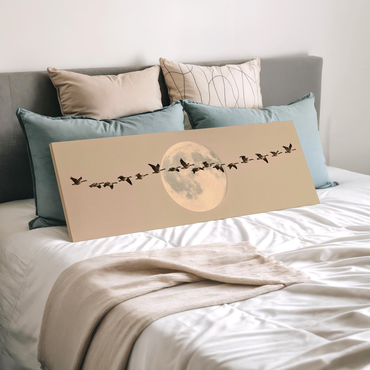 Geese flying across a pale moon on sand wide panoramic canvas print laid on a bed to show its size