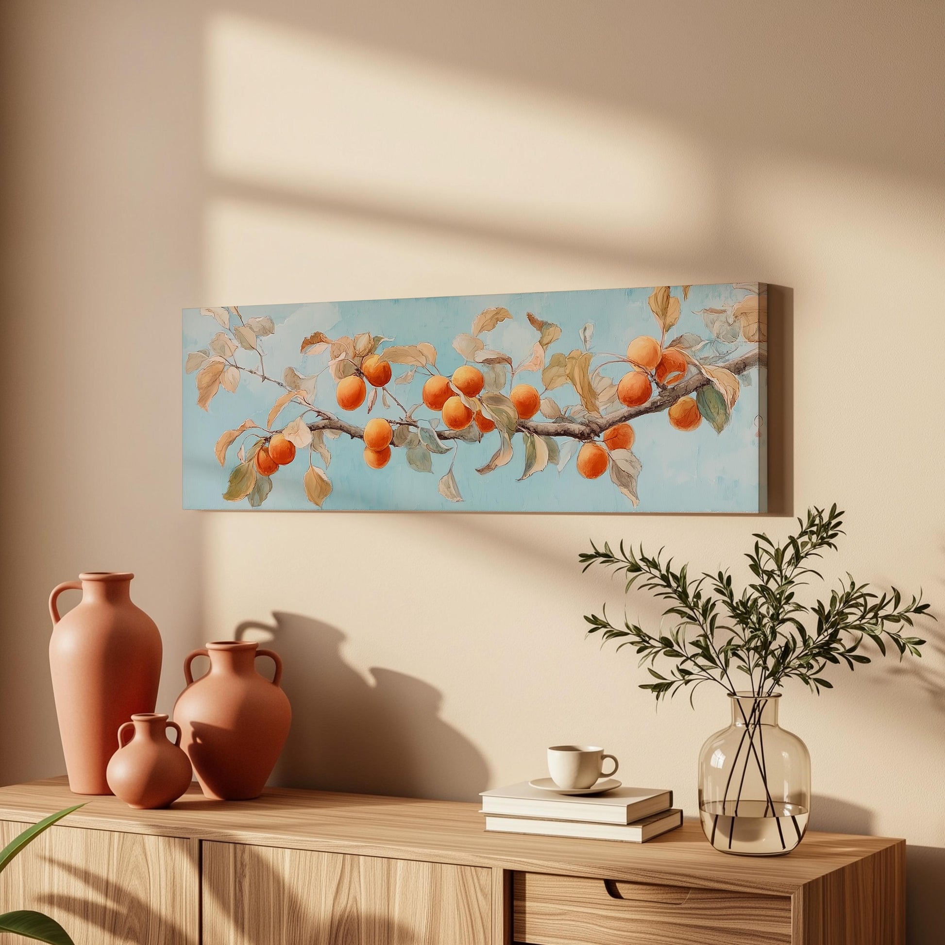 a wooden cabinet with a vase, a plant, and a stack of books on top. Above the cabinet, there is a painting of a branch with orange fruits.