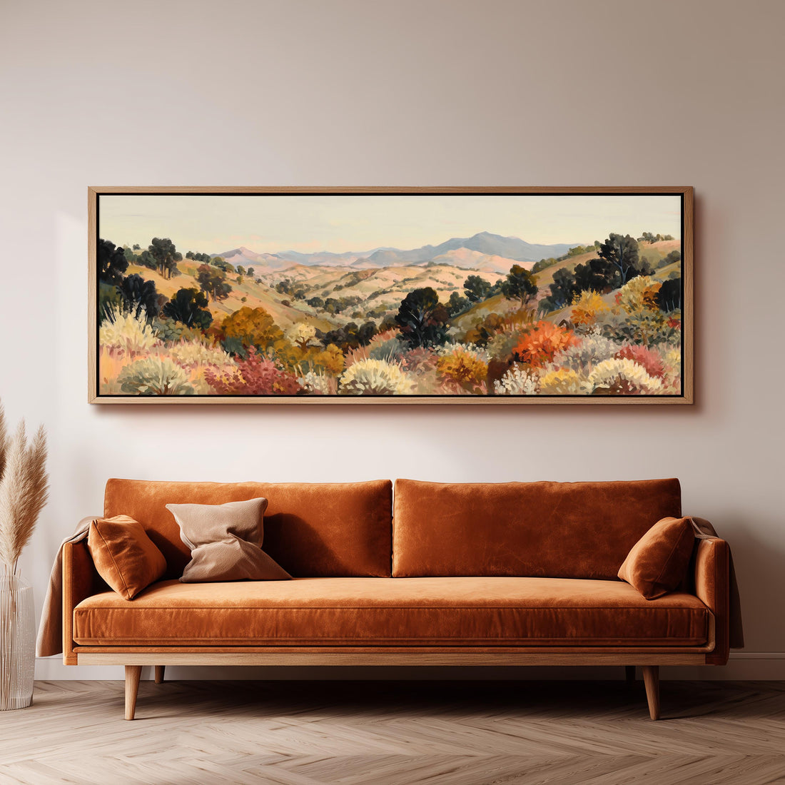 a large, framed painting of a mountainous landscape hanging on a wall above a brown sofa with orange cushions.