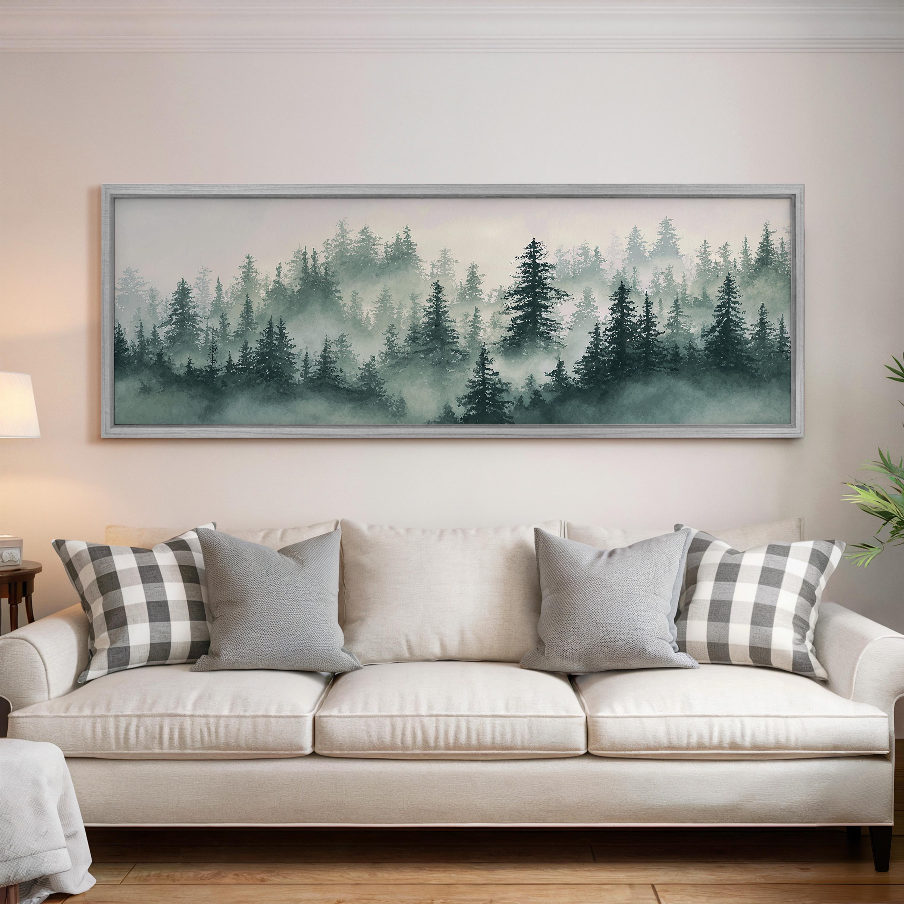 a large framed painting of a forest scene hanging on a wall above a white sofa with gray and white plaid throw pillows.