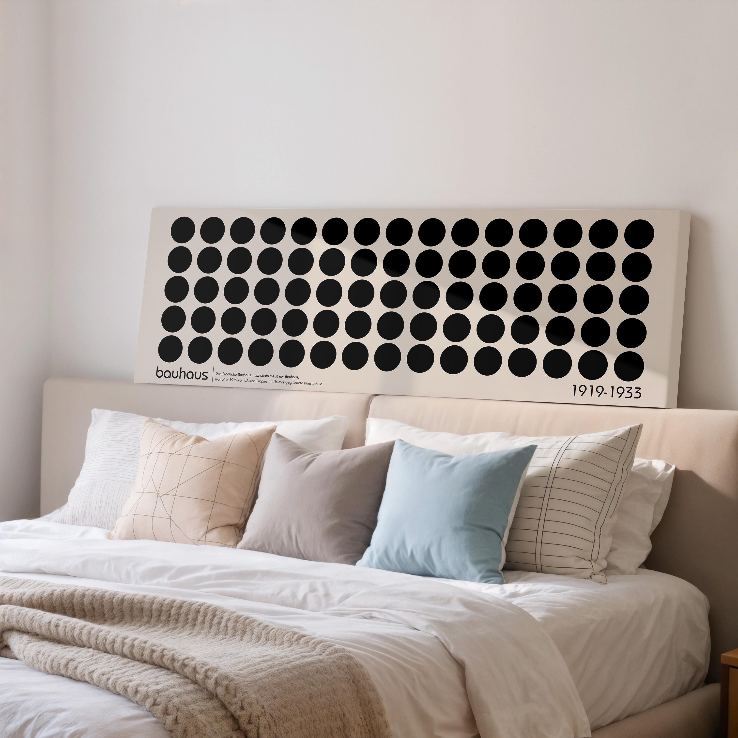 a large bed with a white comforter and various pillows, including a blue pillow. Above the bed, there is a large canvas or poster with a repeating pattern of black circles on a white background.