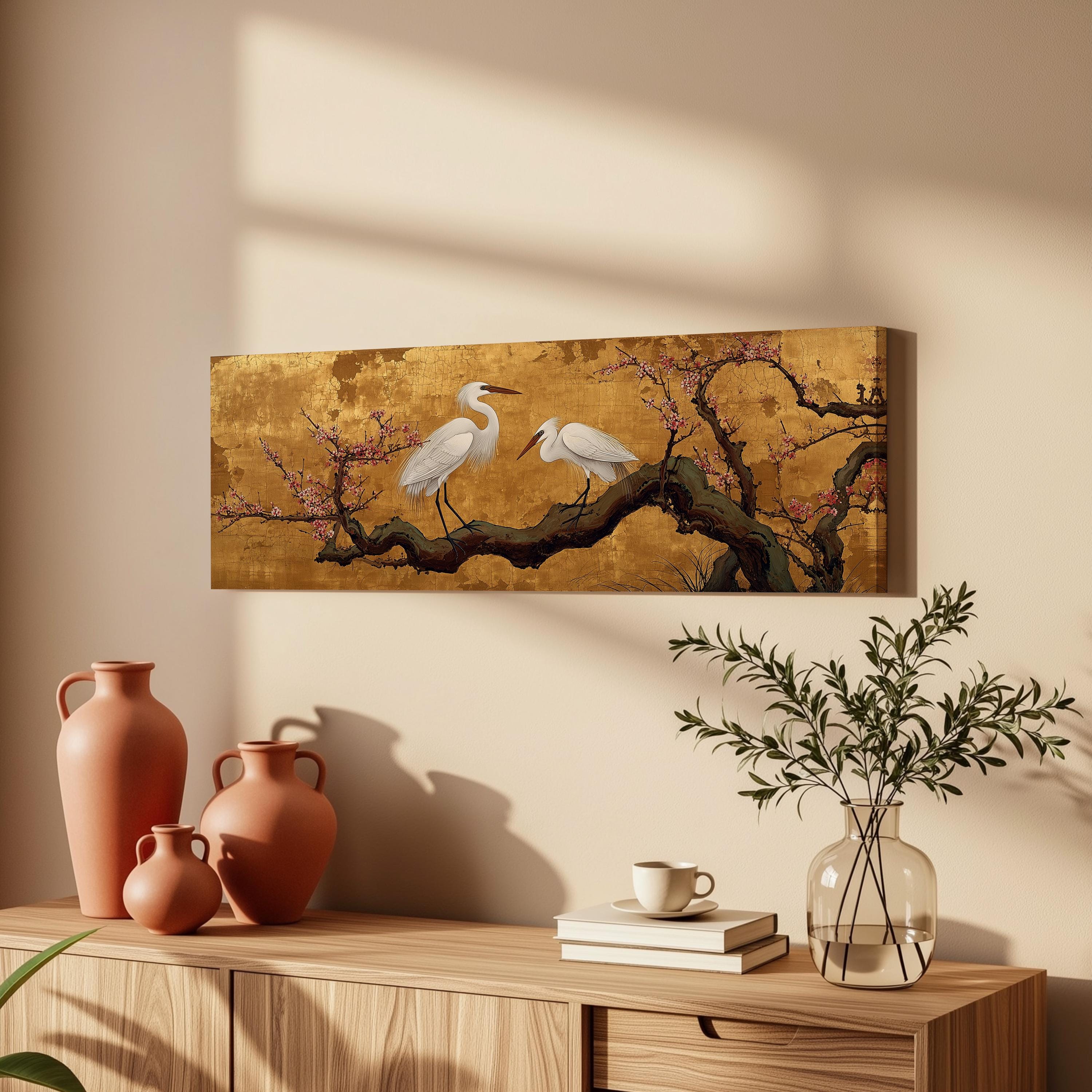 a wooden cabinet with a painting of two white birds perched on a branch, a vase with greenery, and a stack of books.