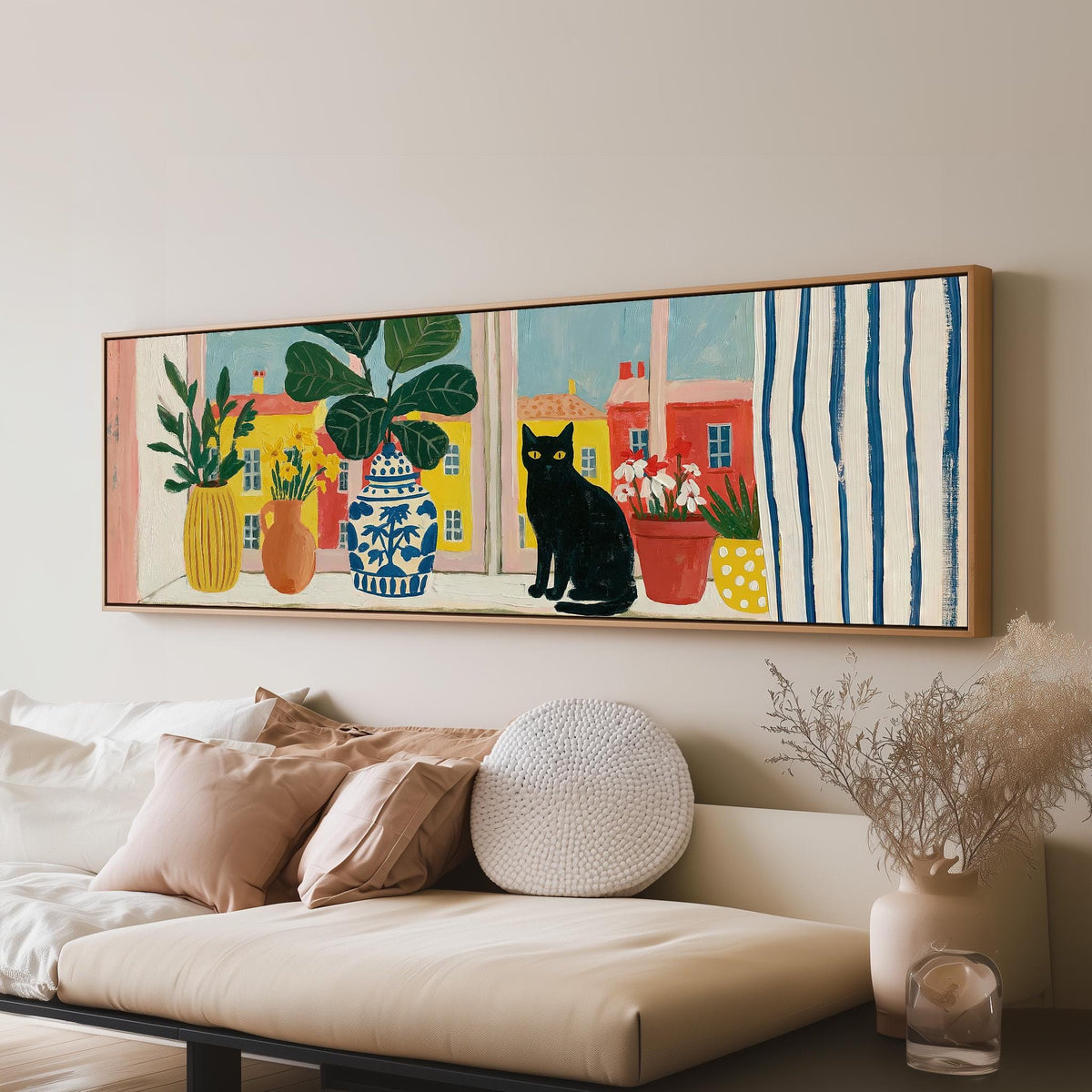 Black cat on a windowsill overlooking a colorful village panoramic canvas print above a sofa in a living room