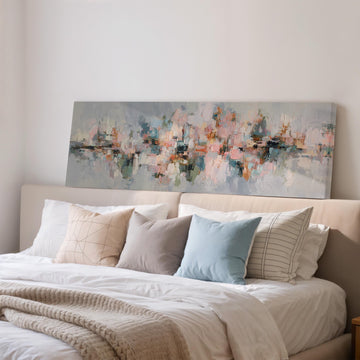 a large abstract painting hanging on a wall above a bed with white bedding and various pillows.