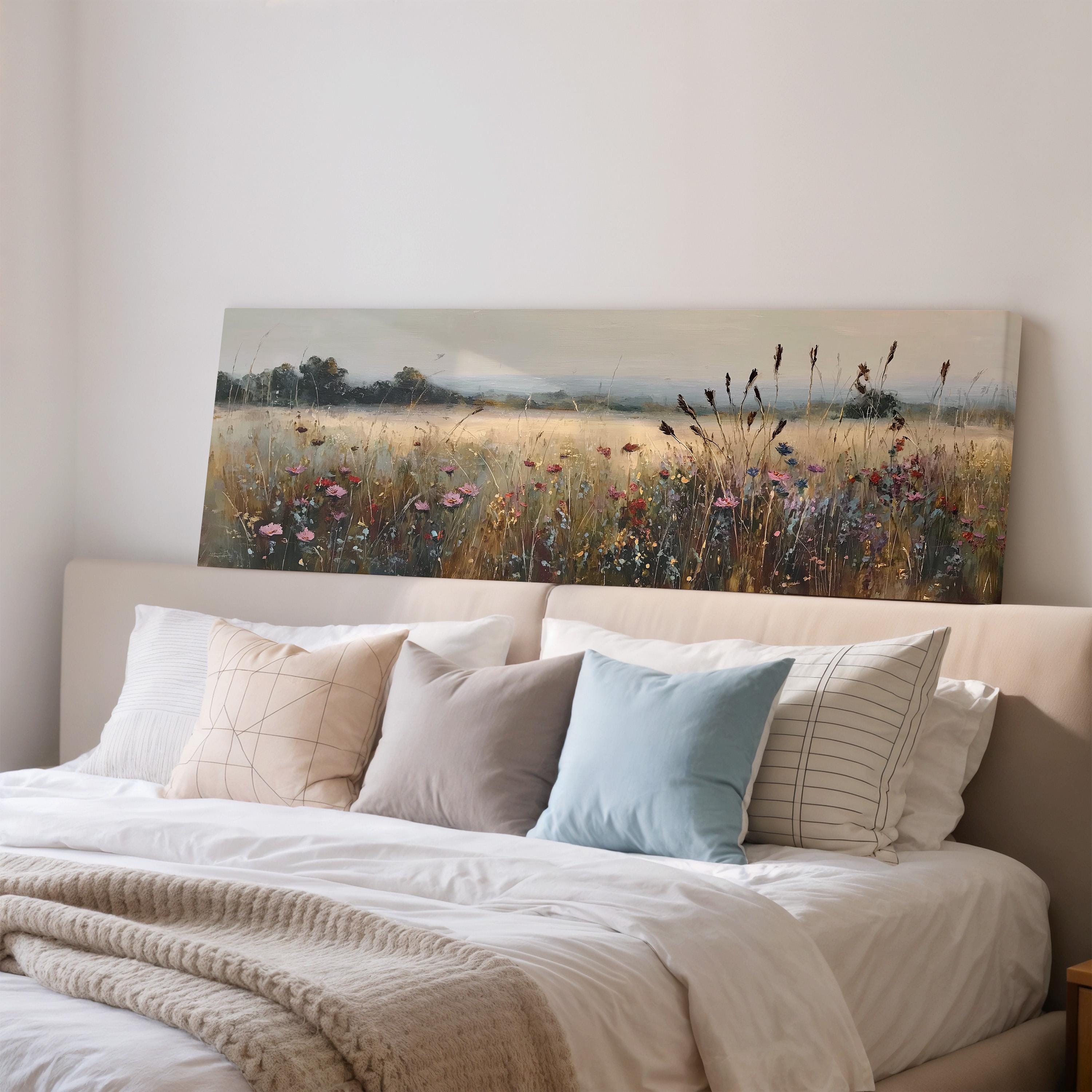 a large painting of a field with flowers hanging above a bed with white linens and pillows.