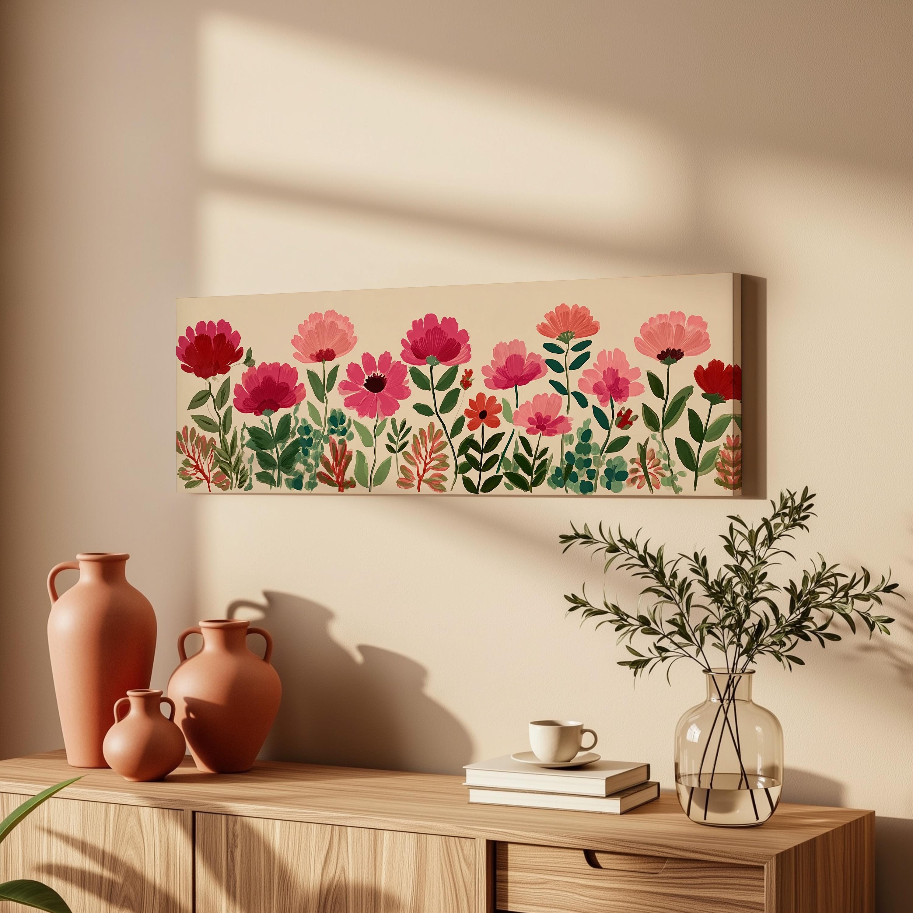 a wooden dresser with a vase of greenery, a coffee cup, and a stack of books. Above the dresser, there is a painting of pink flowers and green leaves.