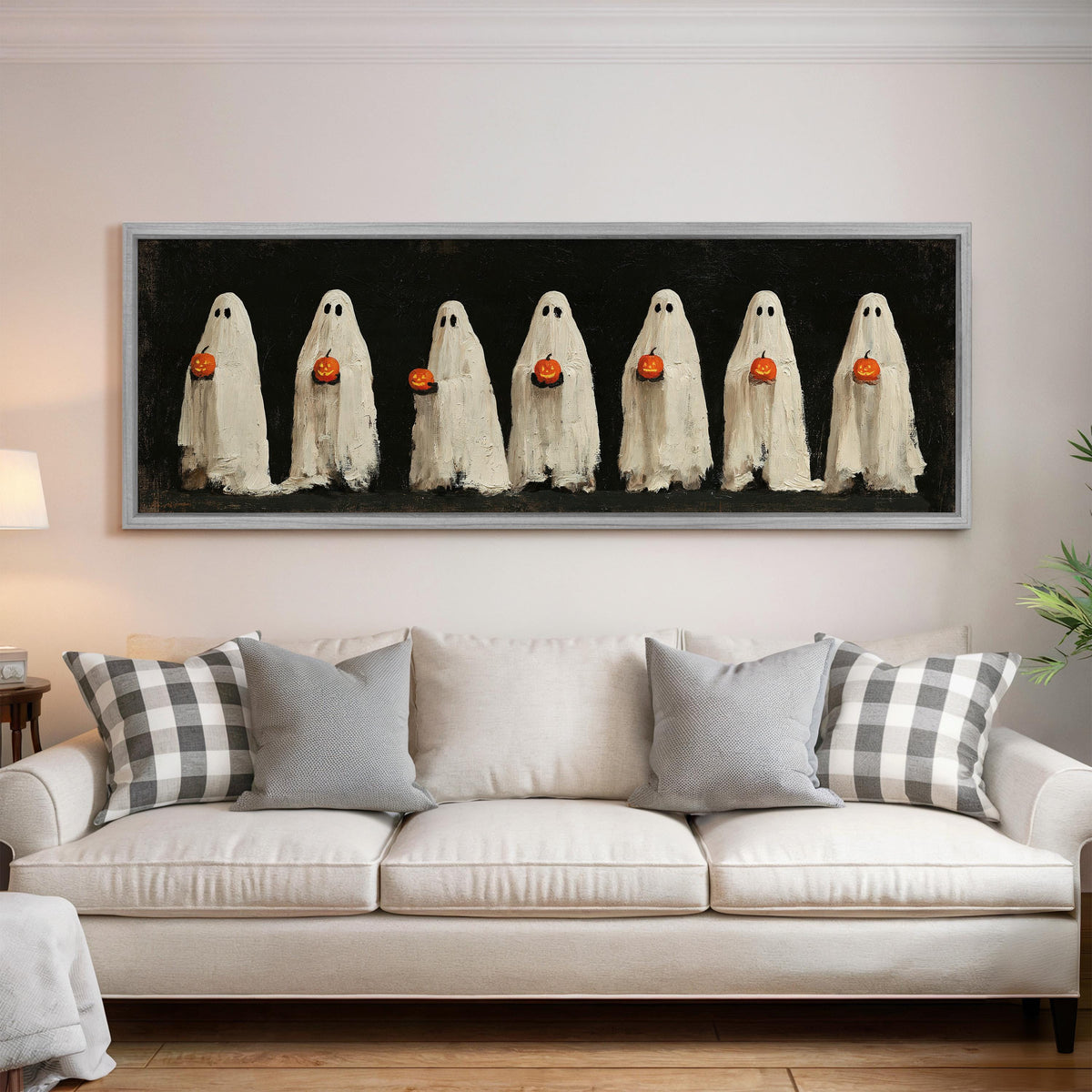 Row of ghosts holding pumpkins panoramic canvas print above a white sofa in a bright living room