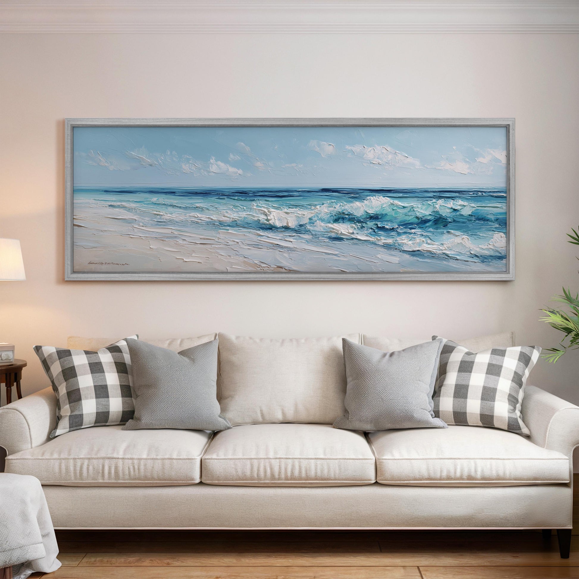 a large painting of a beach scene hanging on a wall above a white sofa with gray and white patterned pillows.