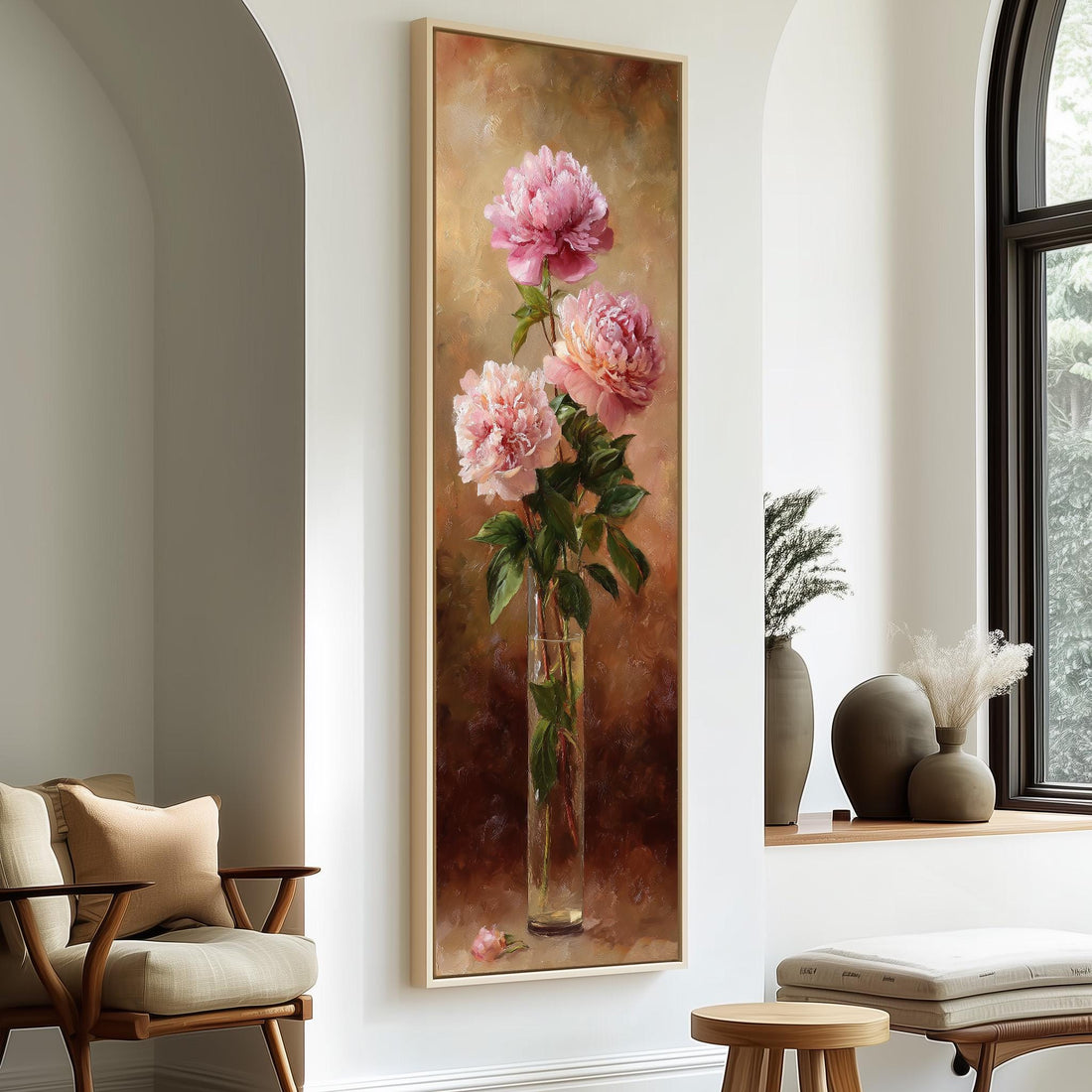 A framed painting of three pink peonies in a vase is hanging on a wall in a room with a wooden cabinet and a window.
