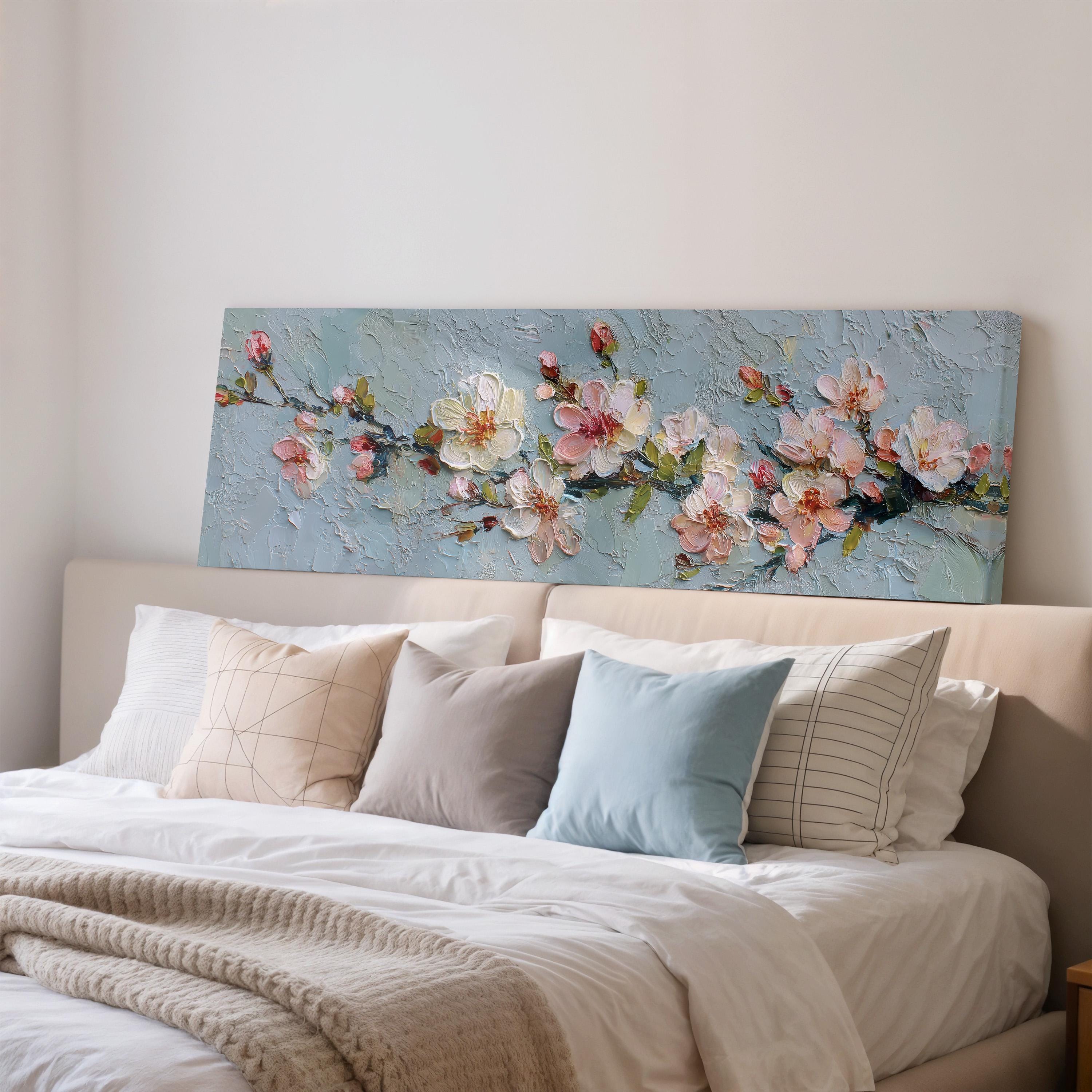 a large painting of flowers on a wall above a bed with white pillows and a gray blanket.