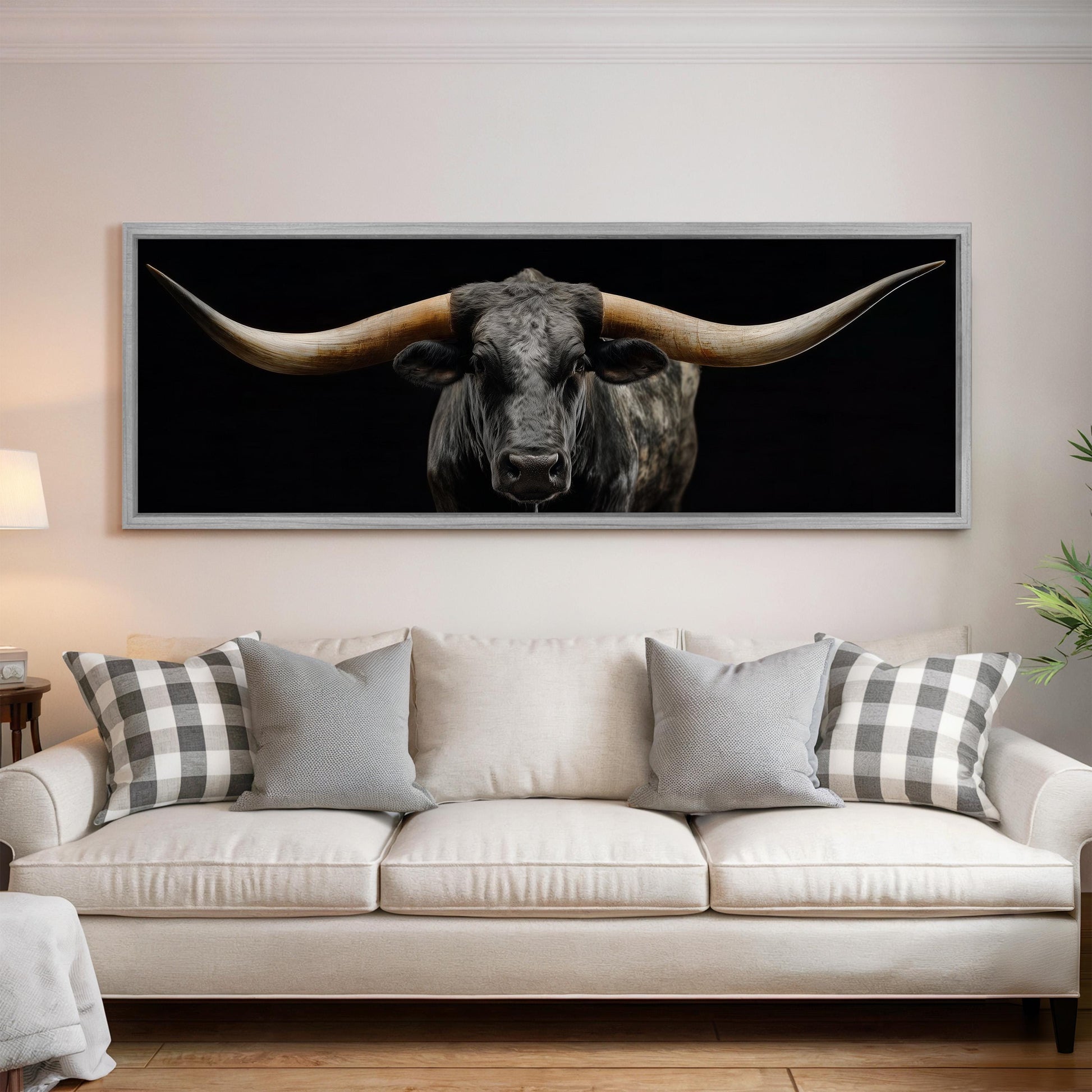 a large framed picture of a bull with long horns hanging on a wall above a white couch in a living room.