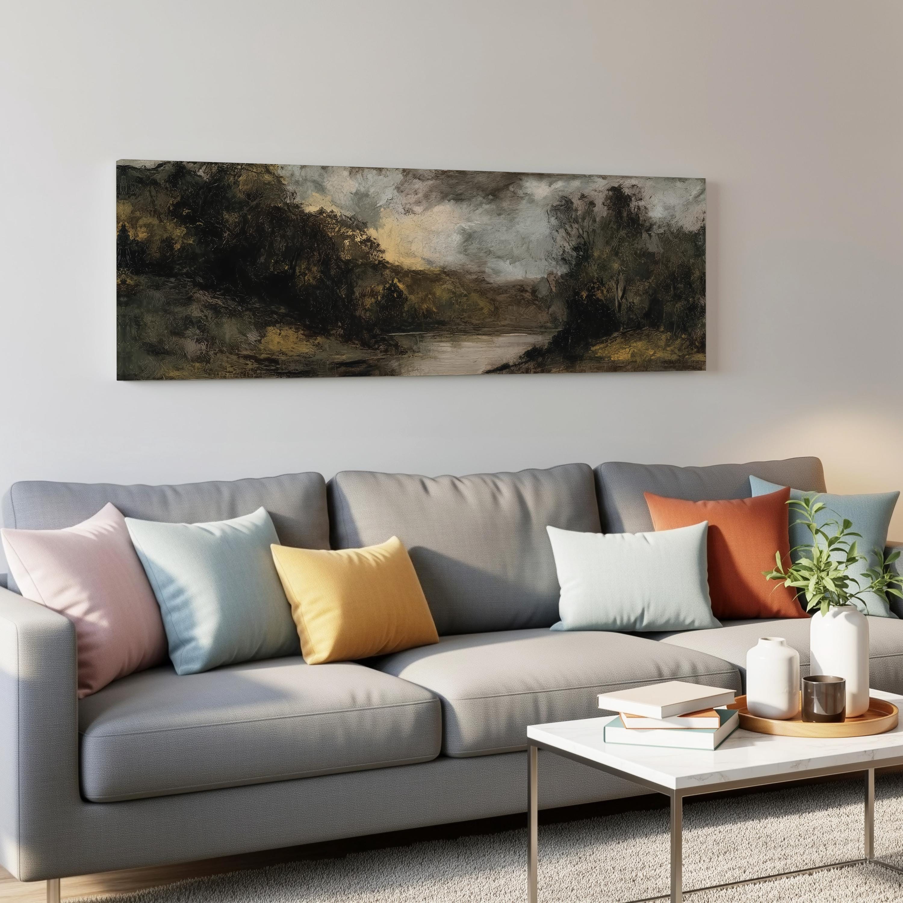 a gray couch with colorful throw pillows, a coffee table with books and a plant, and a large landscape painting hanging on the wall above the couch.