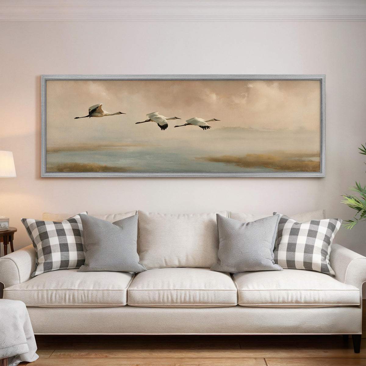 Cranes flying over a calm shore at dusk panoramic canvas print above a white sofa in a bright living room